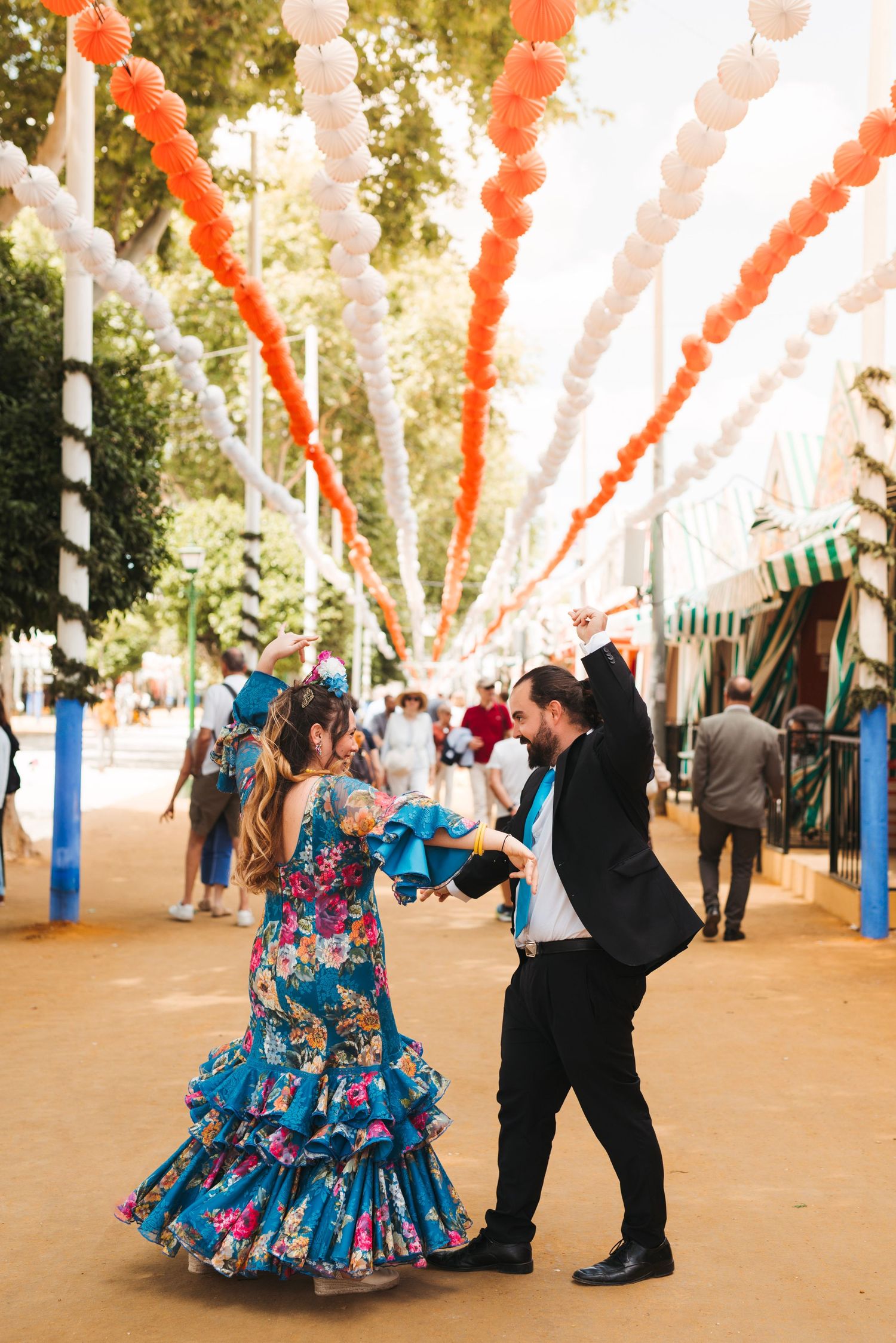 Couple dancing flamenco in traditional costumes under red and white lanterns at Seville fair.