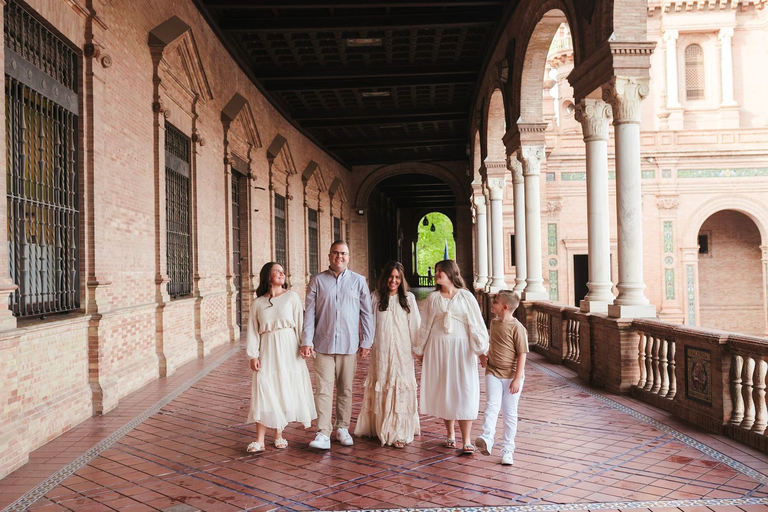 A family of five walking together along a beautiful arched corridor at Plaza de España, Seville.