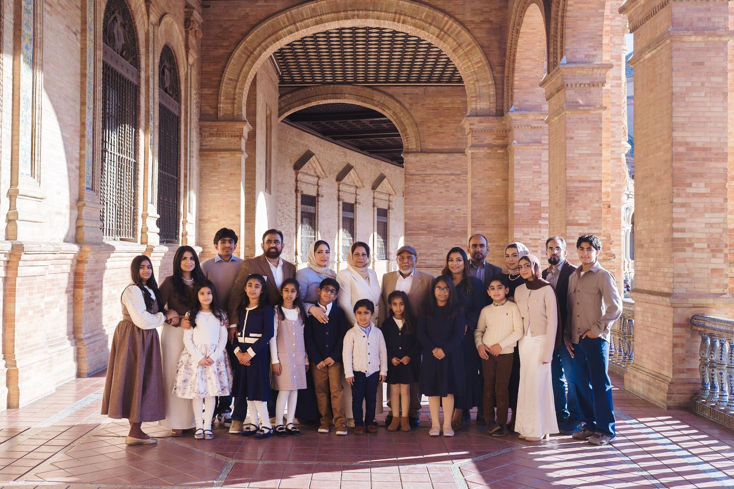 A large extended family group posing together under the arched colonnade at Plaza de España, Seville.
