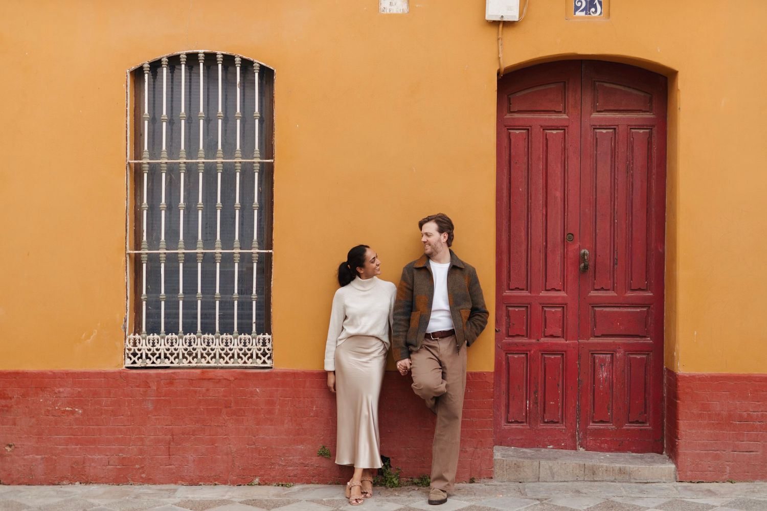 Stylish couple laughing together against a vibrant yellow and red wall with a classic red door.