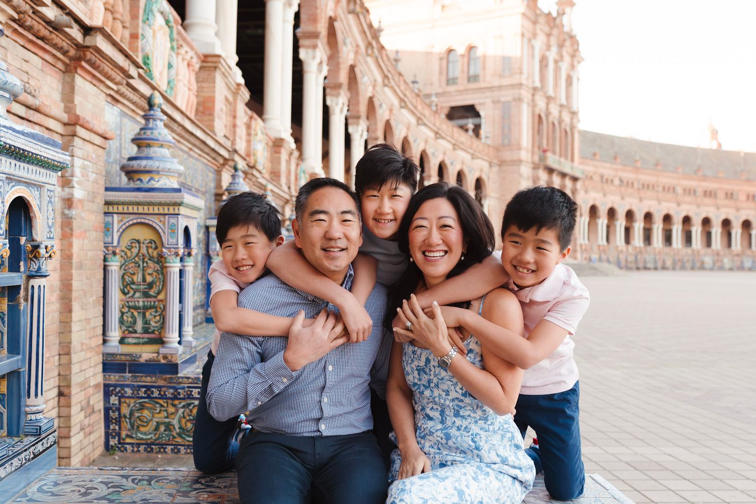 A joyful Asian family of five hugging and laughing at the ornate Plaza de Espana in Seville.