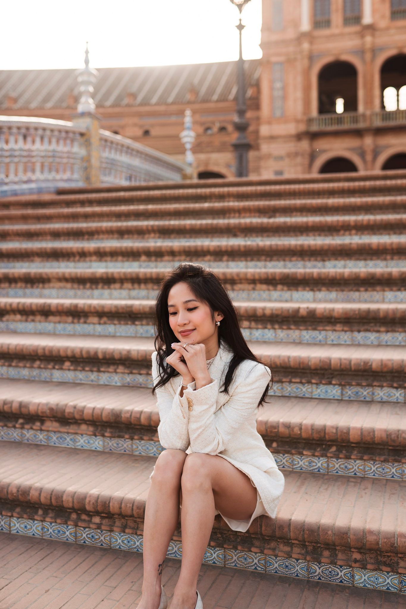 Woman in white dress sitting on tiled steps at Plaza de España, Seville.