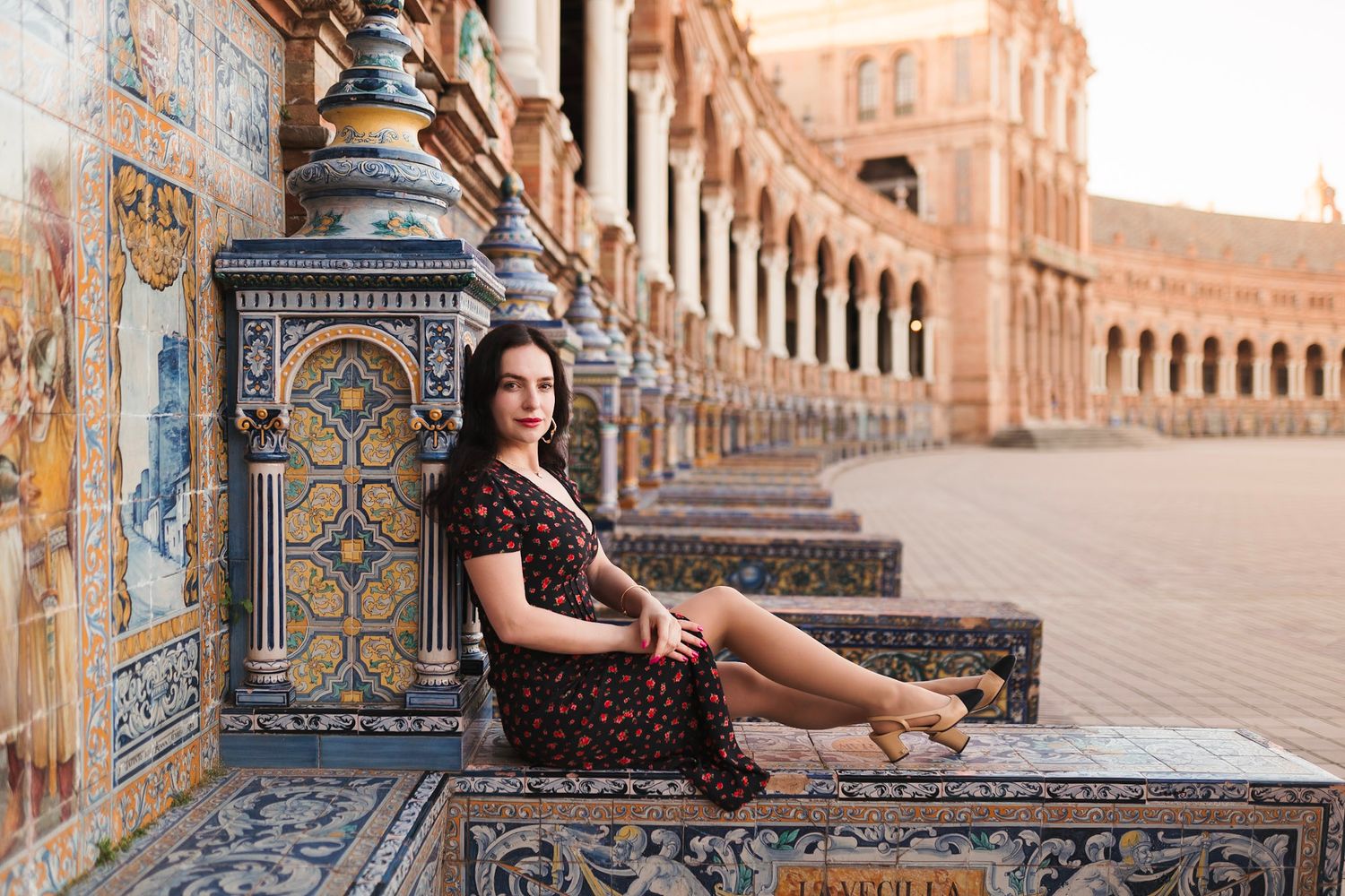 Woman in floral dress sits on ornate tiled bench at Plaza de España, Seville, Spain.