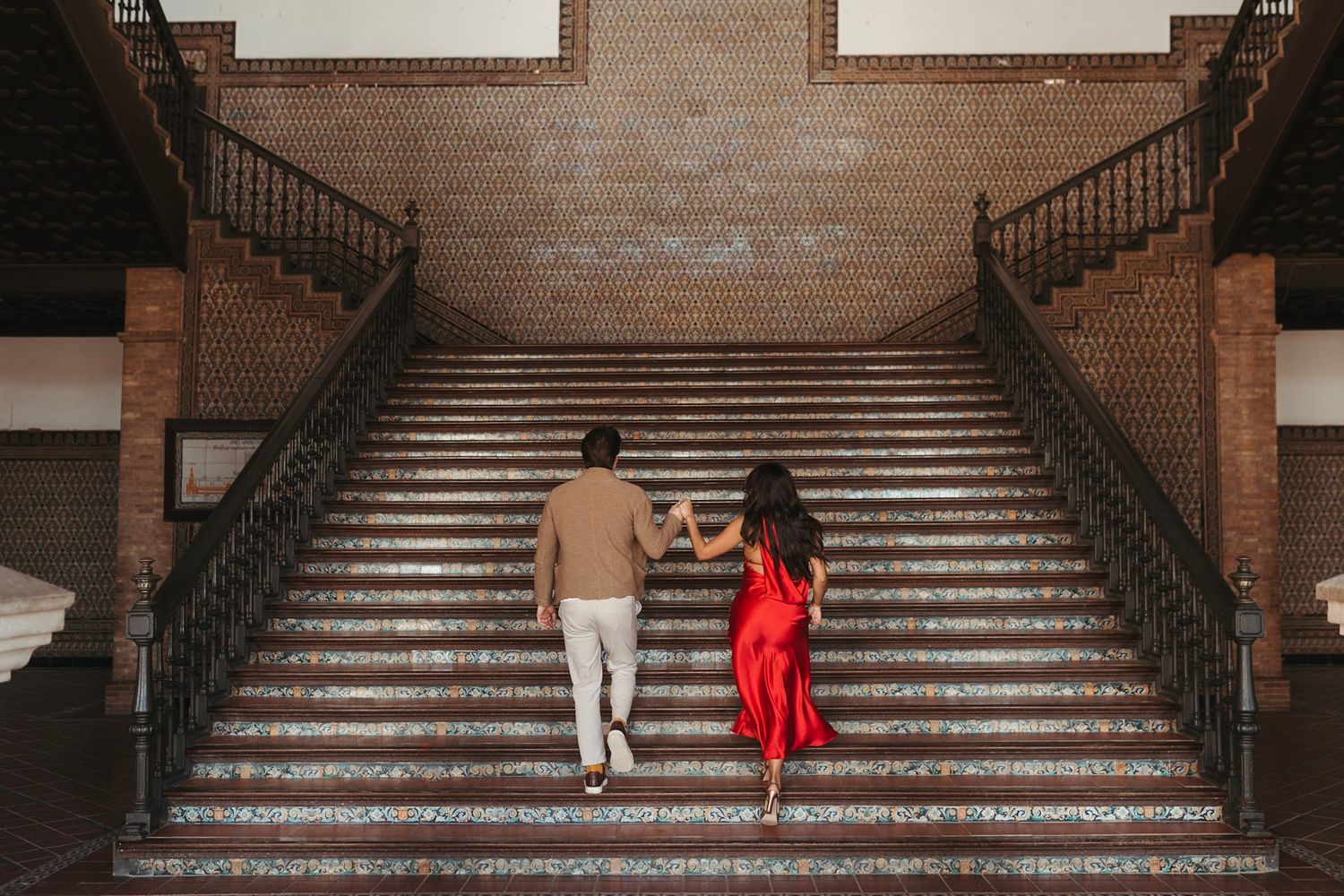 Couple walking up ornate brick stairs hand in hand, viewed from behind.