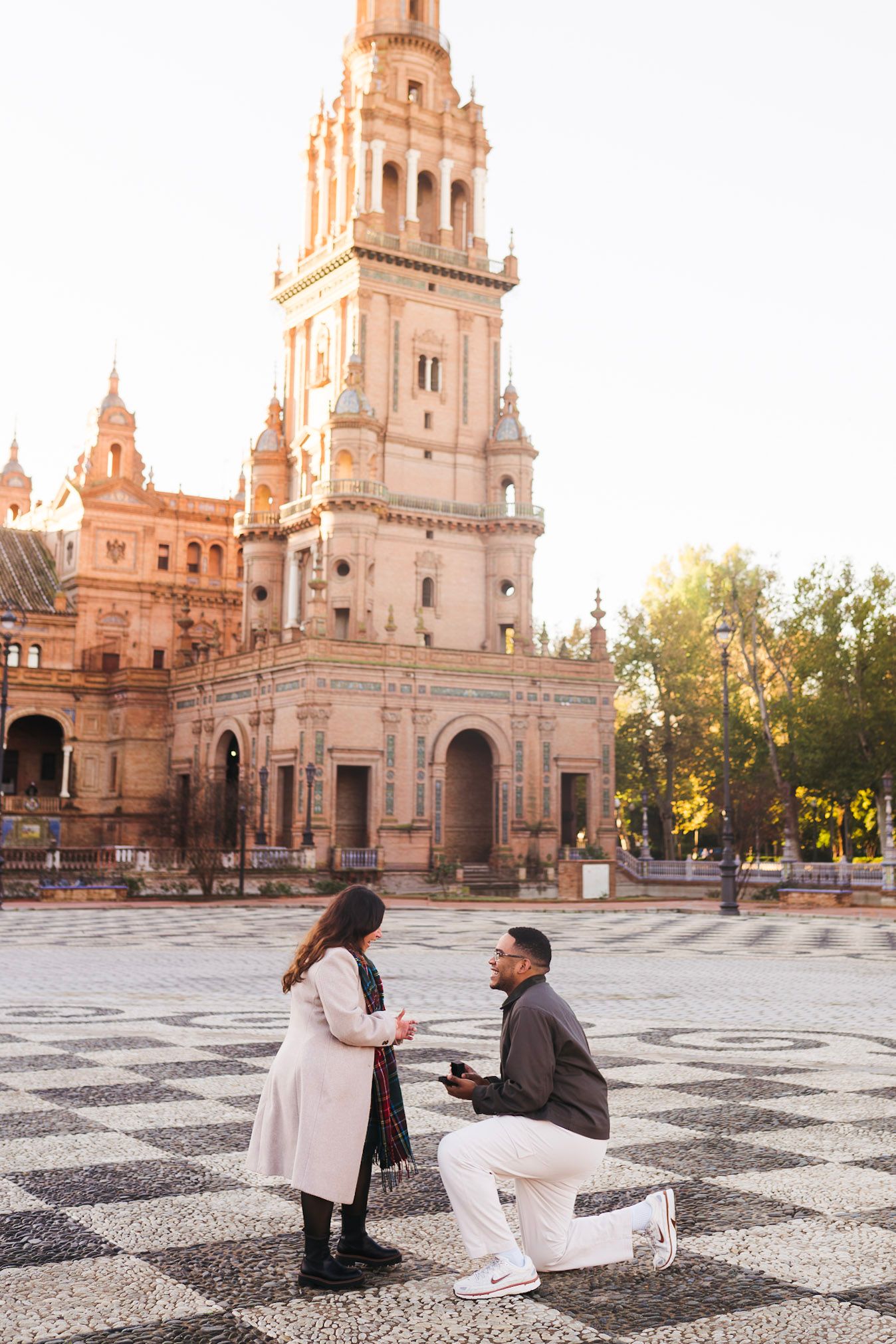 Romantic marriage proposal at Plaza de España Seville with ornate tower backdrop at sunset.