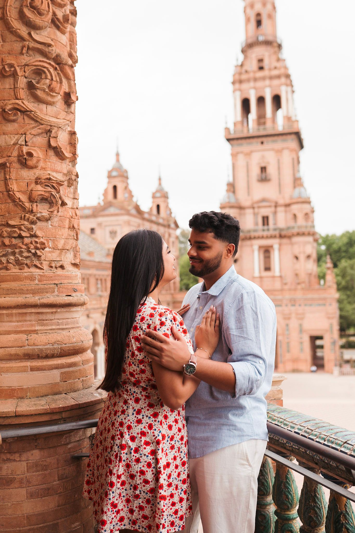 Couple sharing a tender embrace beside an ornate column at Plaza de España in Seville, Spain.