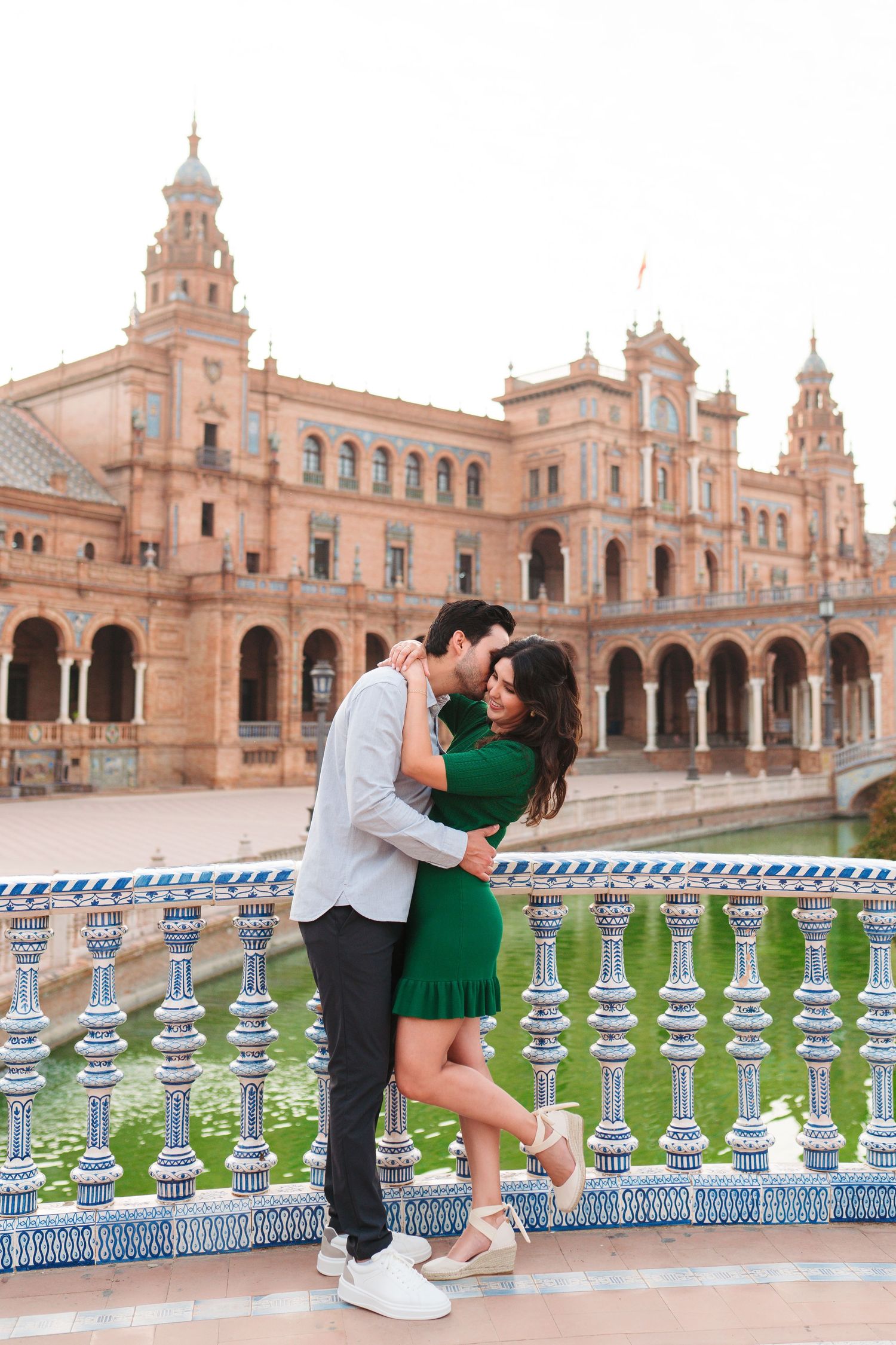 Couple embracing and kissing in front of the iconic Plaza de España in Seville, Spain.