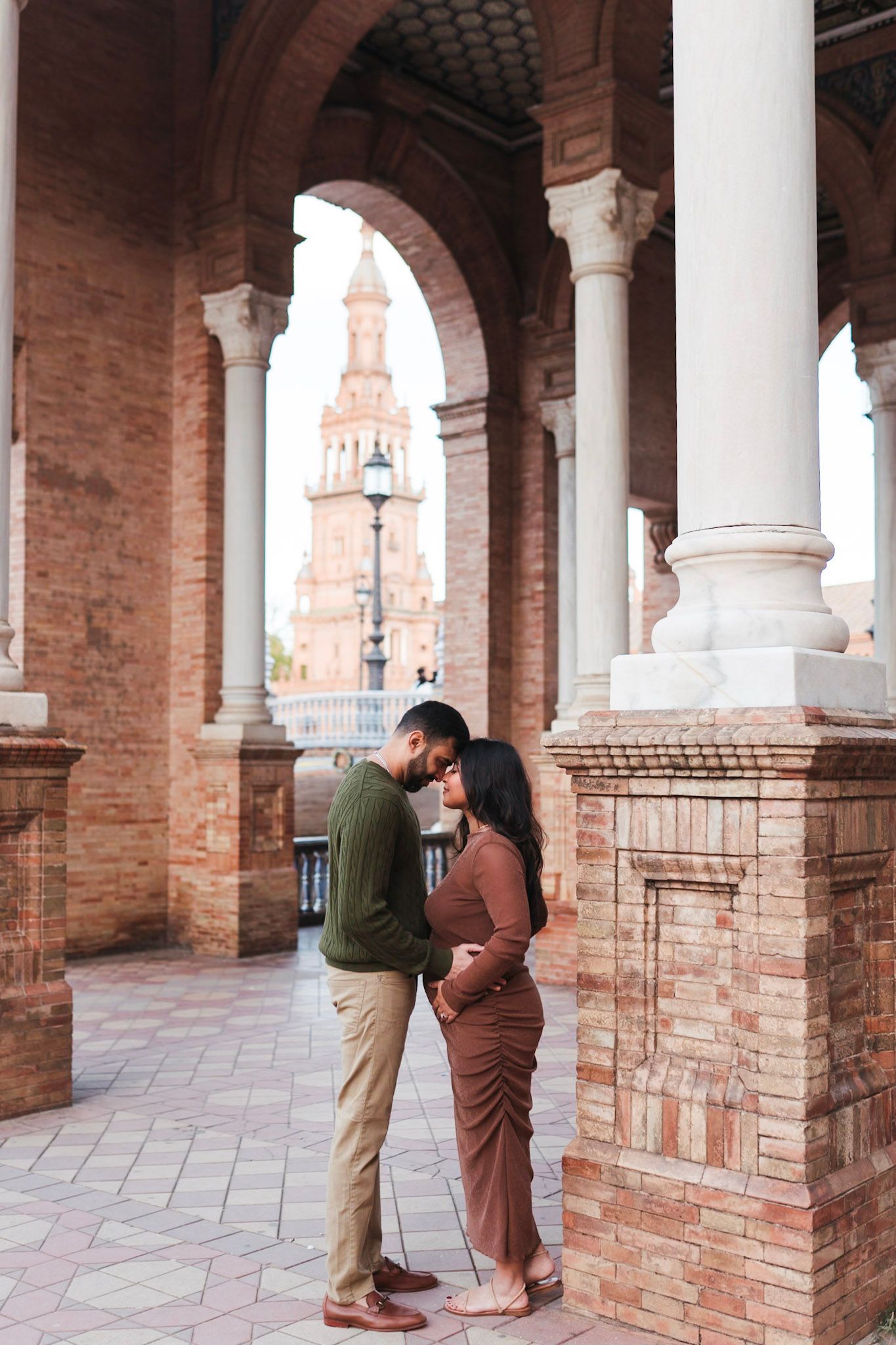 Expecting couple embracing under arches at Plaza de España Seville maternity shoot.