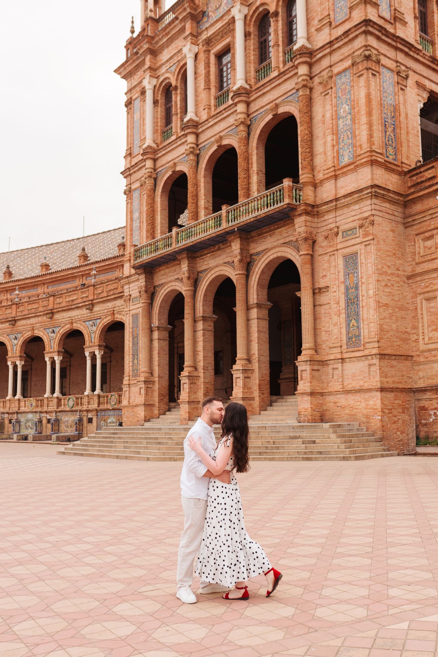 Couple dancing romantically in front of the ornate brick arches of Plaza de España in Seville, Spain.