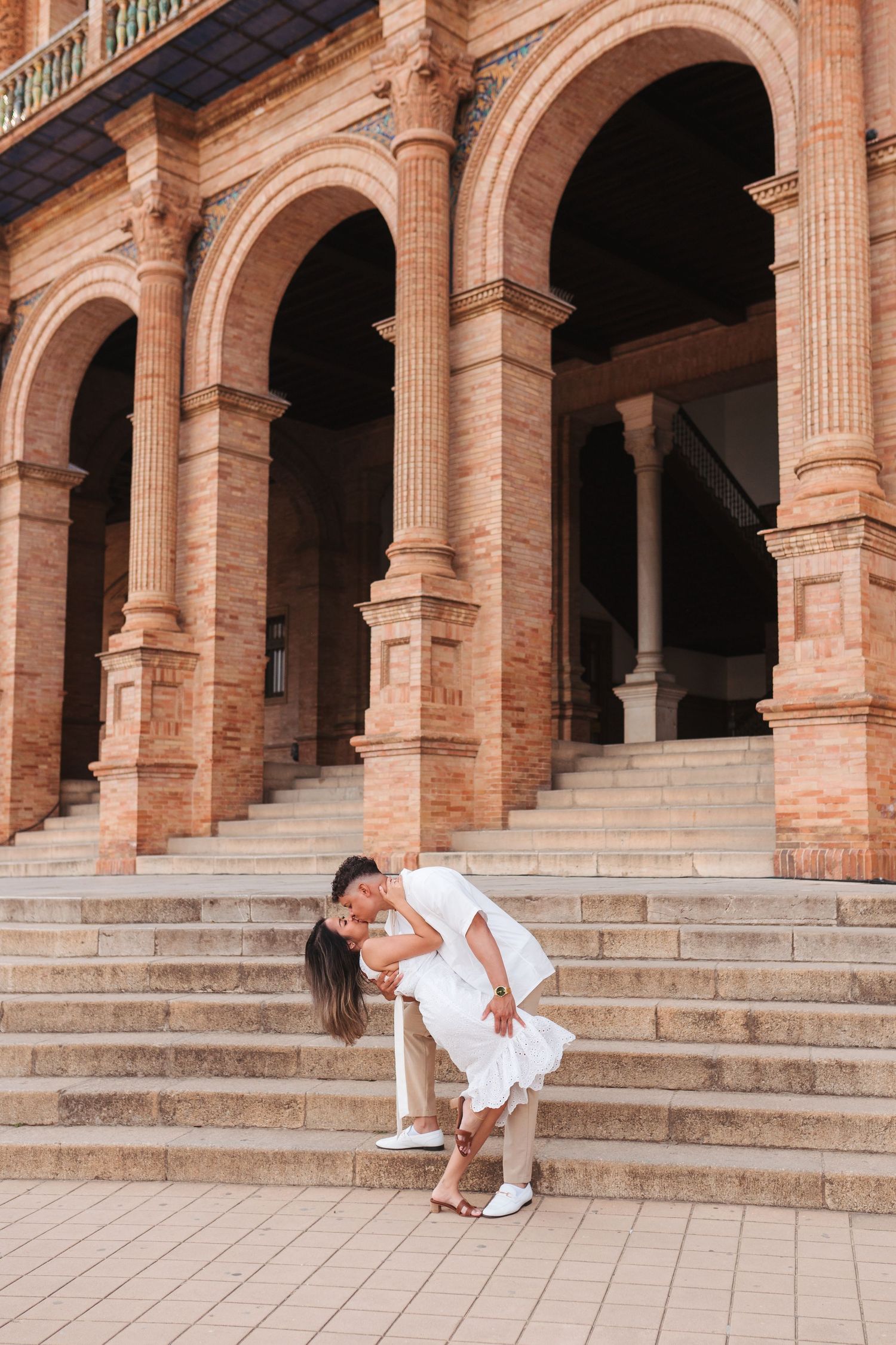 Man dipping woman in white dress for a kiss on steps of Plaza de España, Seville.