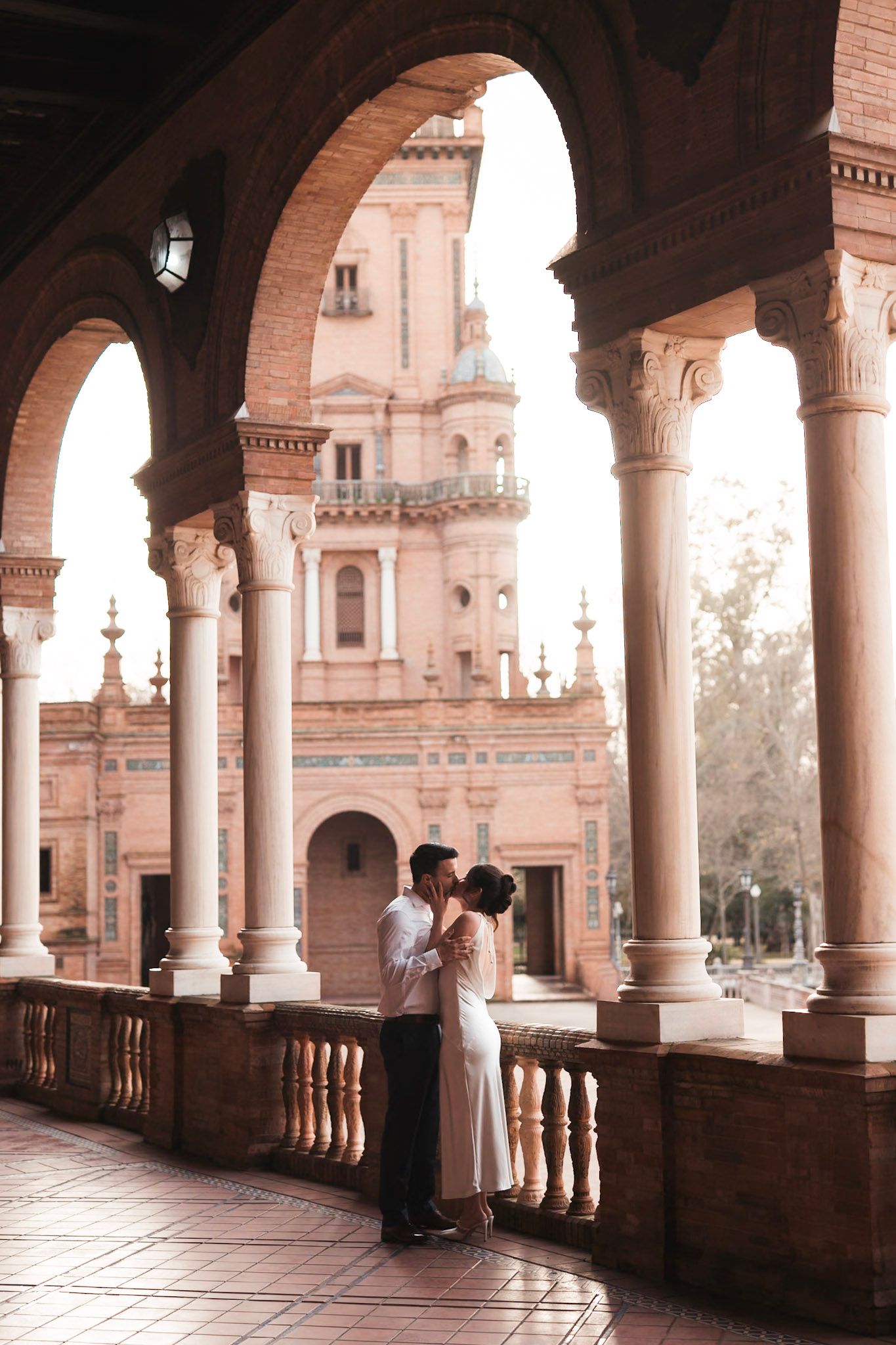 Couple embracing under elegant arched colonnade at Plaza de España, Seville.