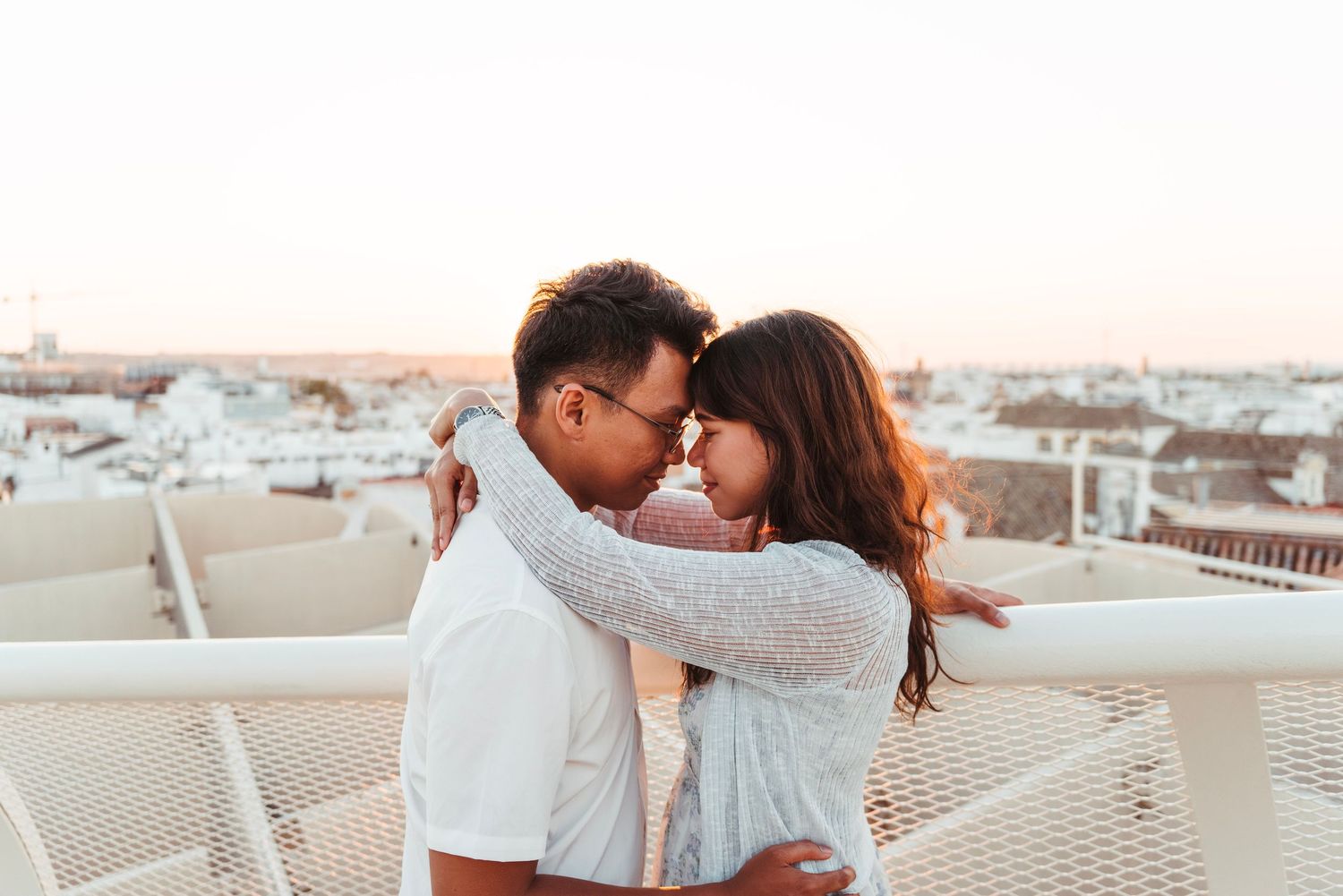 Romantic couple touching foreheads at sunset on Metropol Parasol rooftop overlooking Seville cityscape.