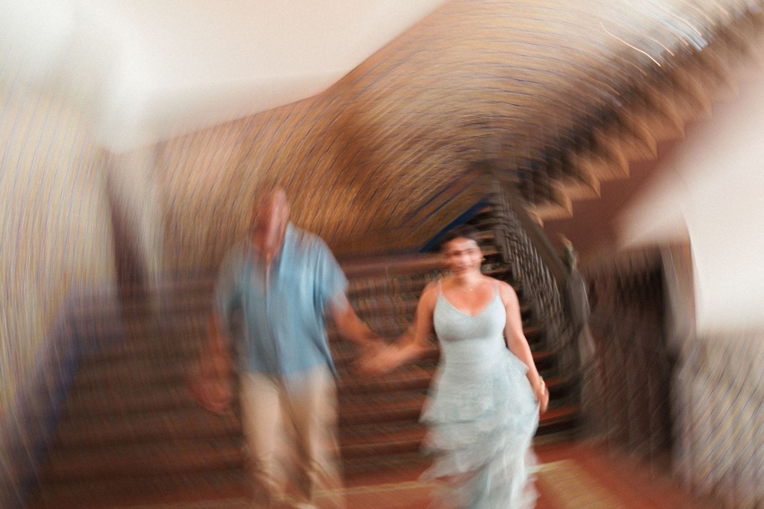 Blurred motion photo of a bride and groom holding hands while walking down a grand staircase on their wedding day.
