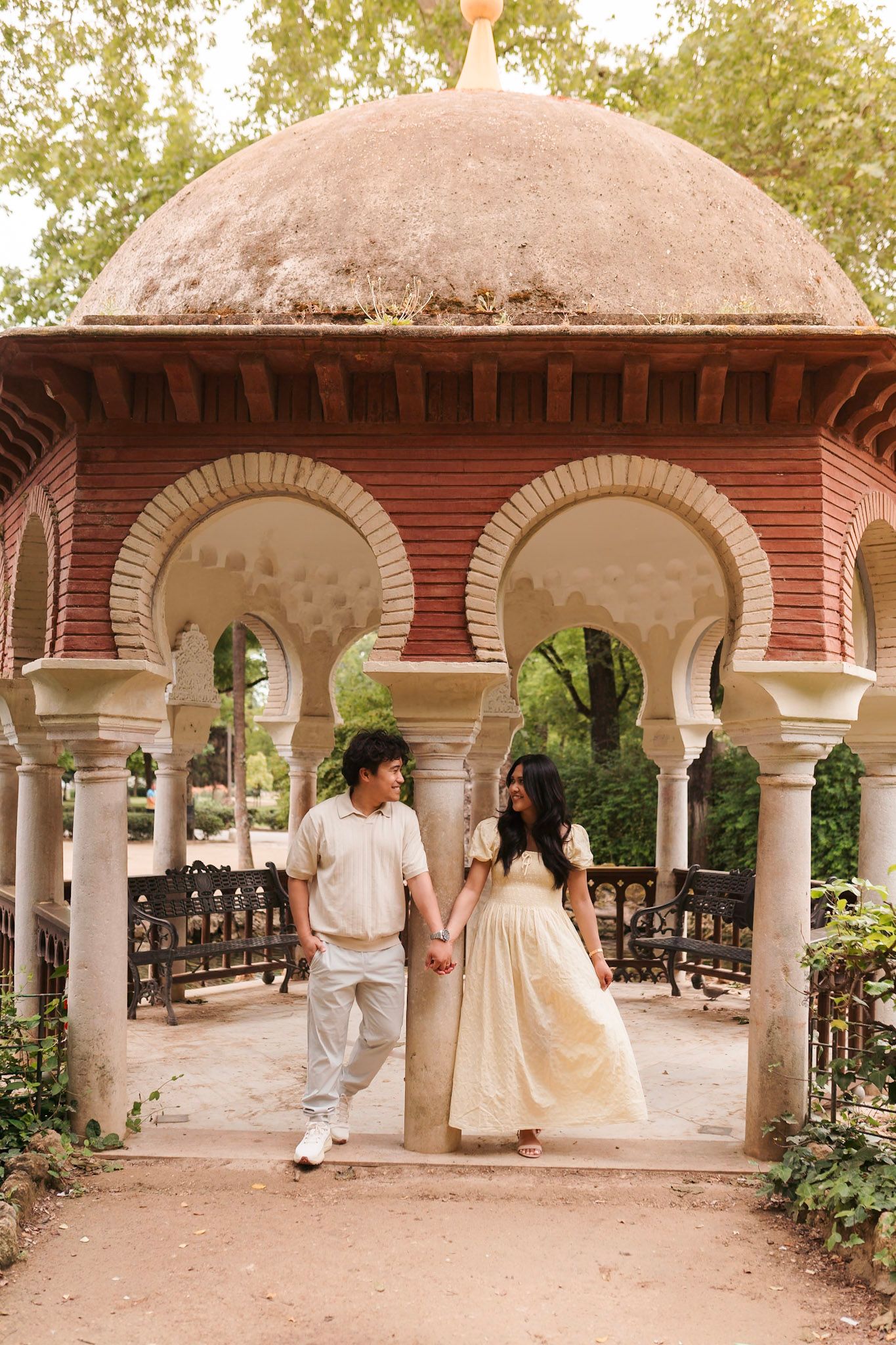 Couple holding hands under ornate Moorish arches of a historic pavilion in a park.