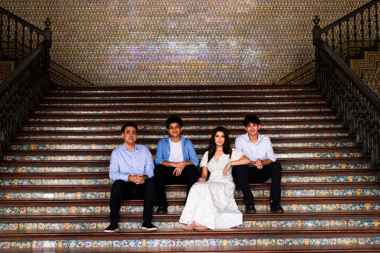 Group of four people sit together on decorative tiled stairs at Plaza de España in Seville.