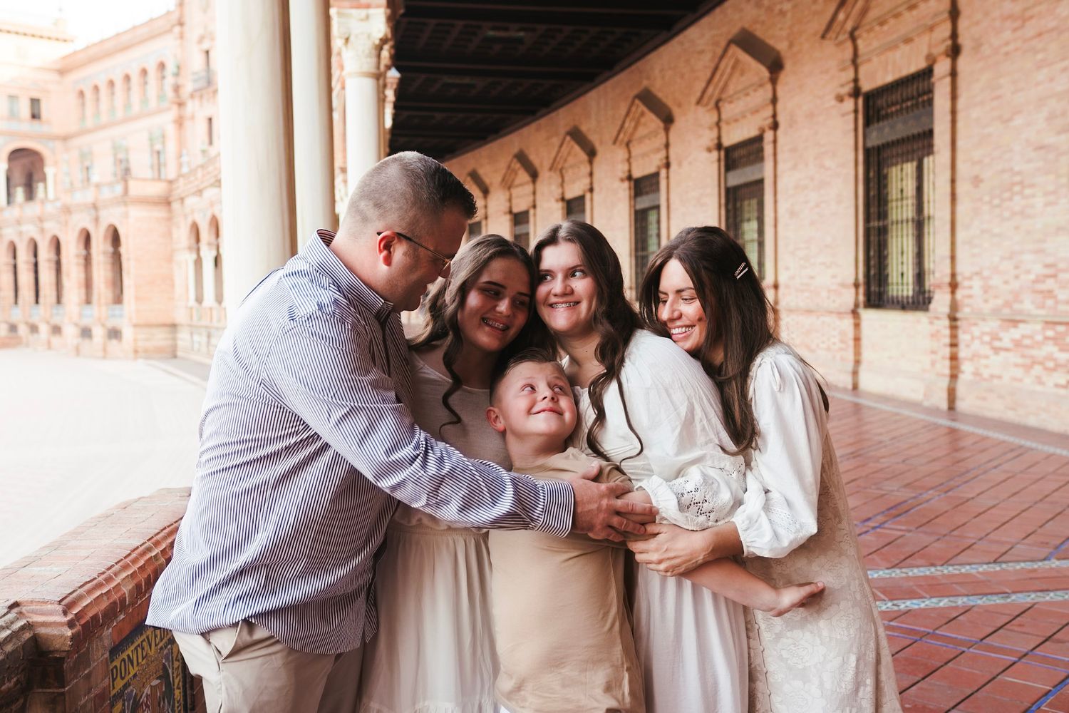 A joyful family hugging and laughing together on a historic arcade in Seville, Spain.