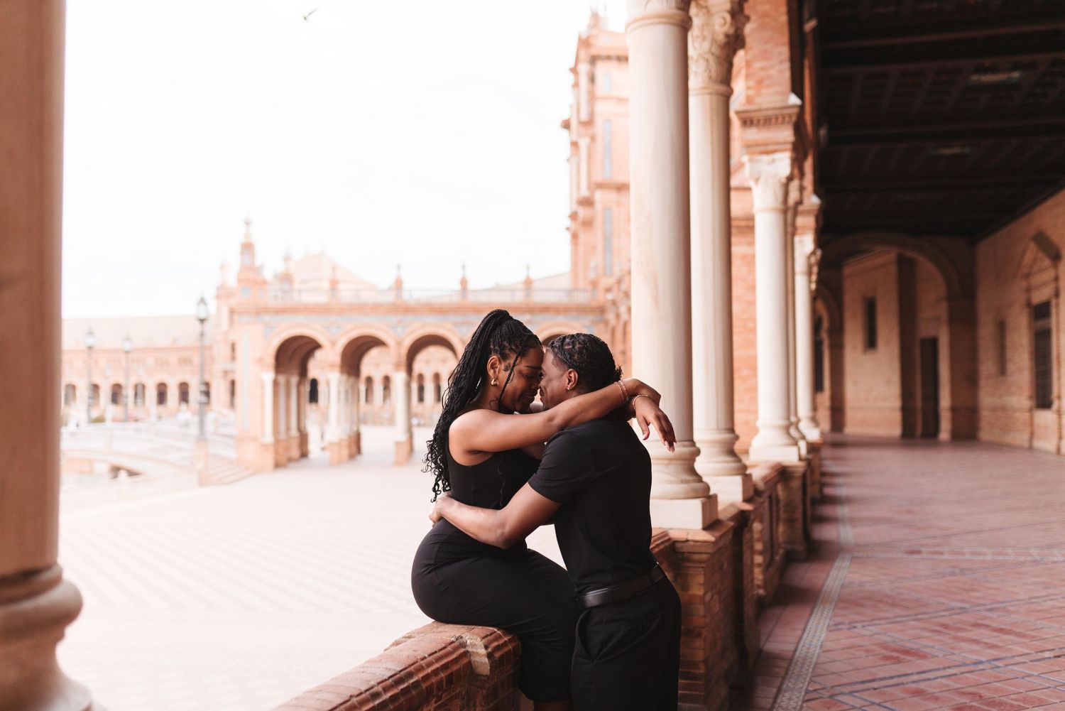 Couple embracing romantically at Plaza de España in Seville, Spain, surrounded by ornate arches and columns.