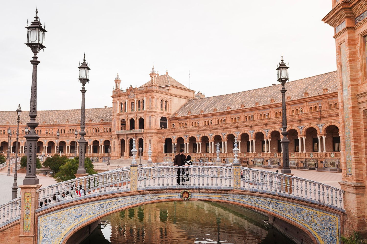 Panoramic view of Plaza de España Seville with ornate bridge over canal and baroque architecture.