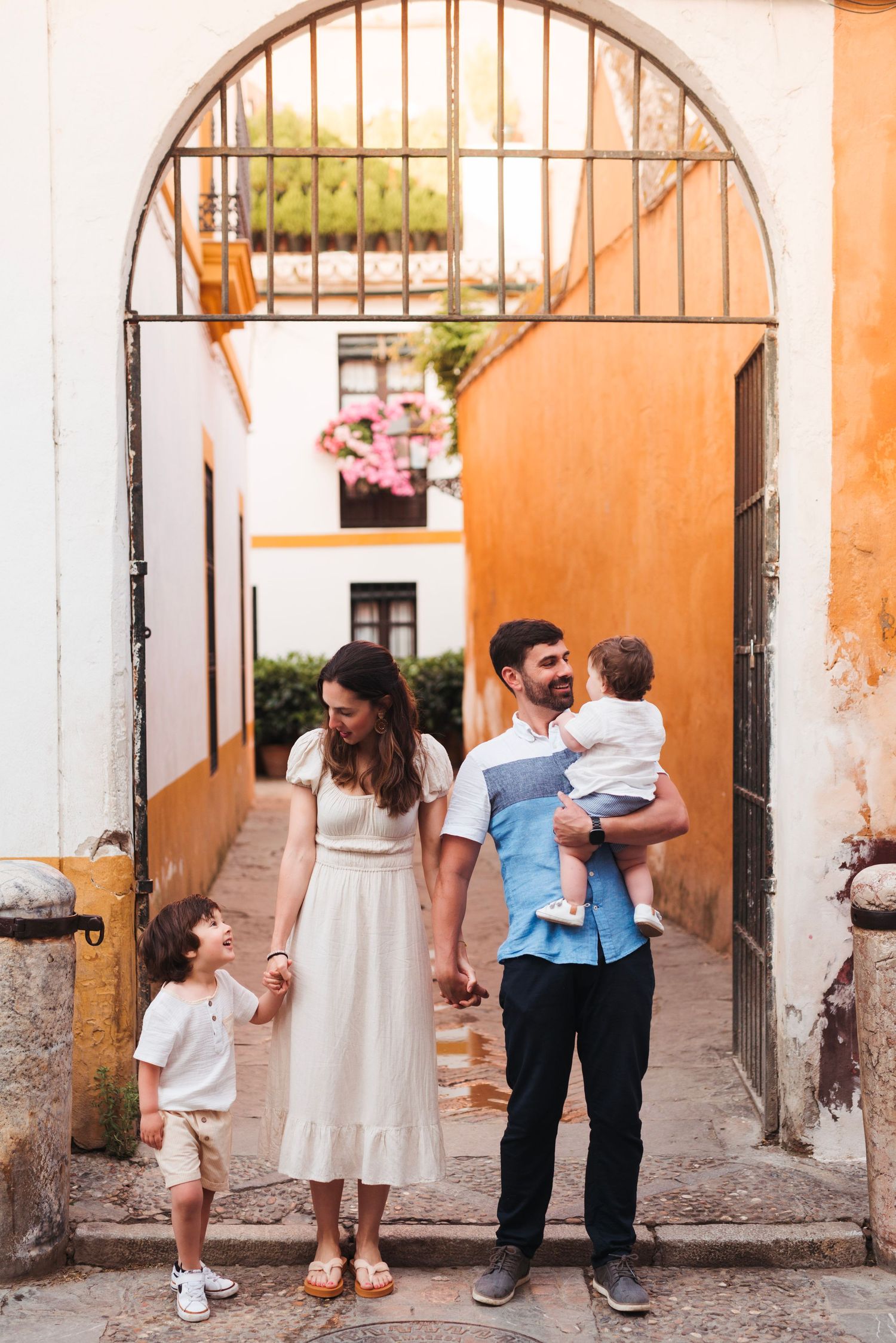Young family with two children standing under arched gateway in colorful Seville alleyway.