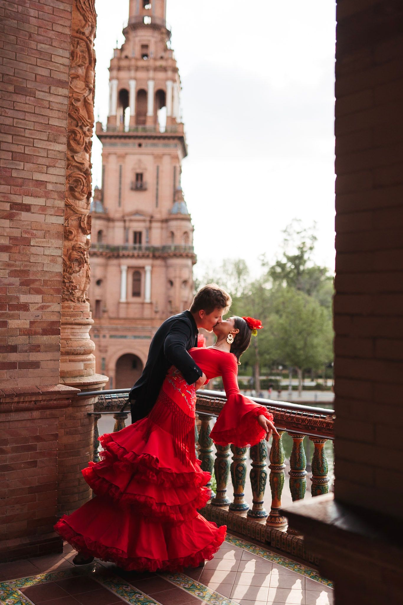 Flamenco couple sharing romantic kiss on balcony at Plaza de España, woman in red ruffled dress.