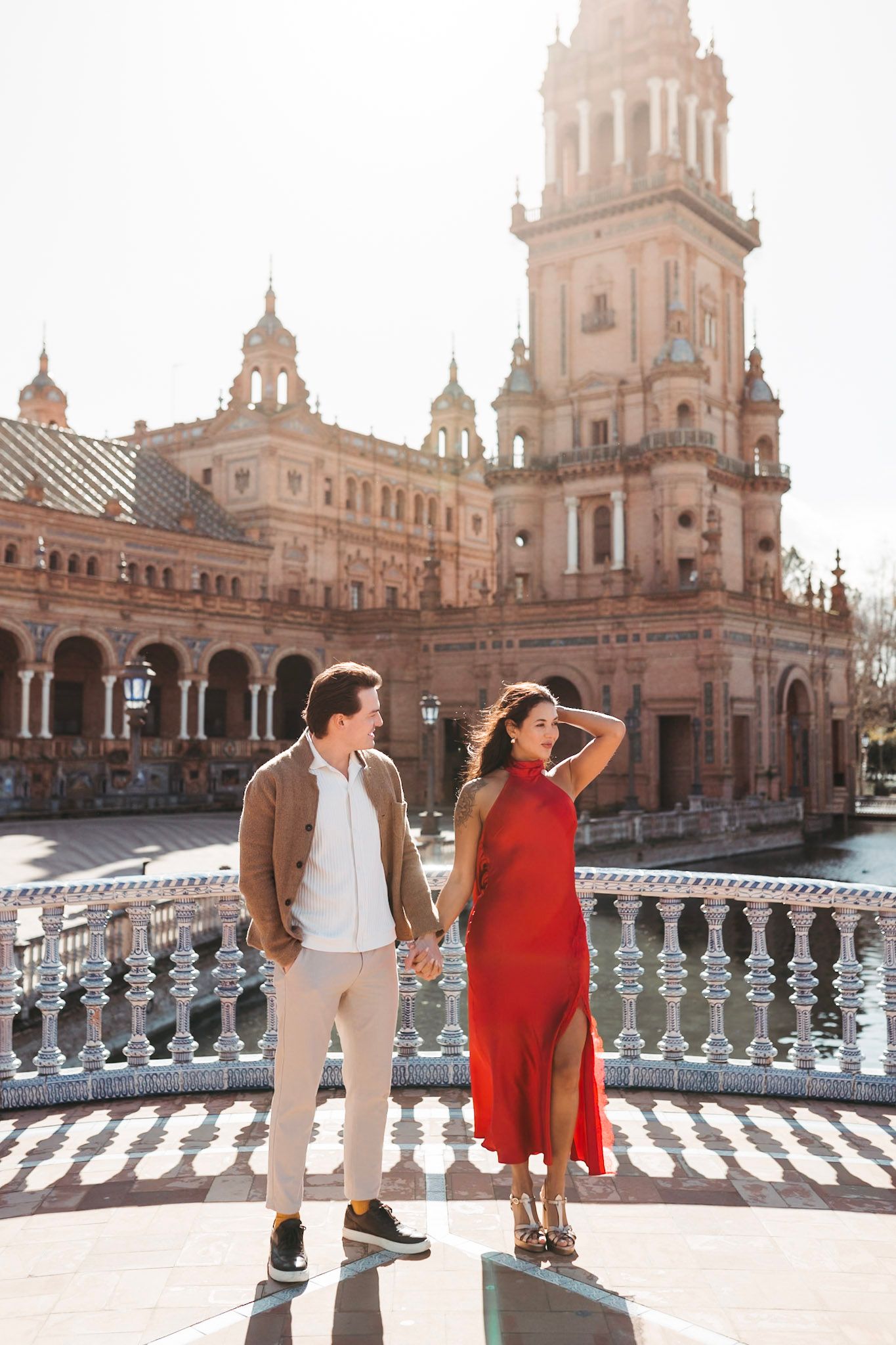 Romantic couple holding hands at Plaza de España, Seville, with iconic tower backdrop.