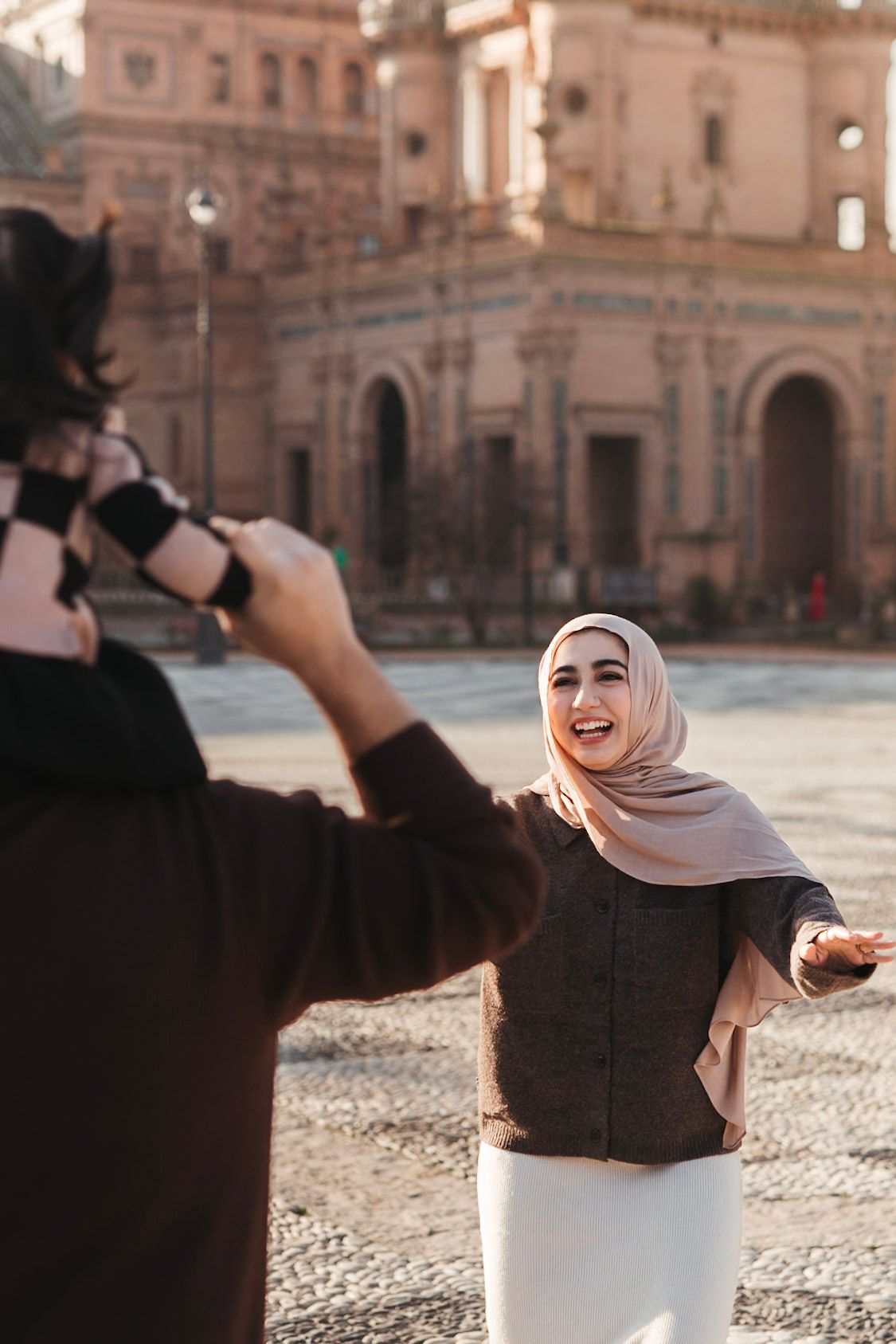 A woman in a hijab laughs joyfully while holding hands with her partner at Plaza de España, Seville.