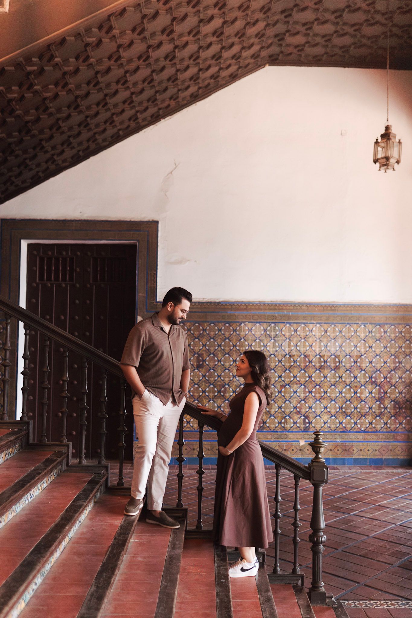 Couple sharing a moment on ornate tiled staircase in historic Spanish building.