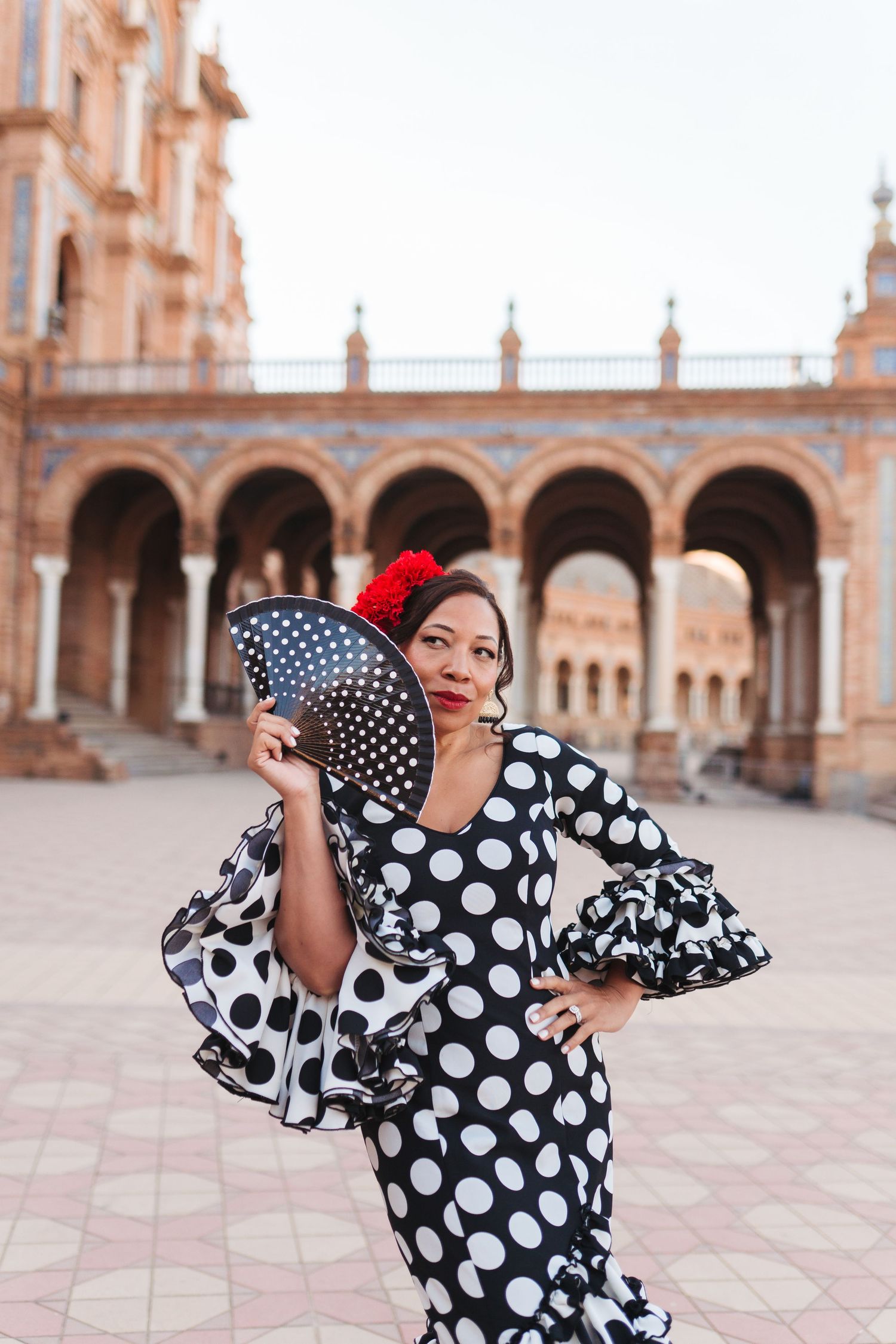 Flamenco dancer in polka dot dress holds fan at Plaza de España, Seville.