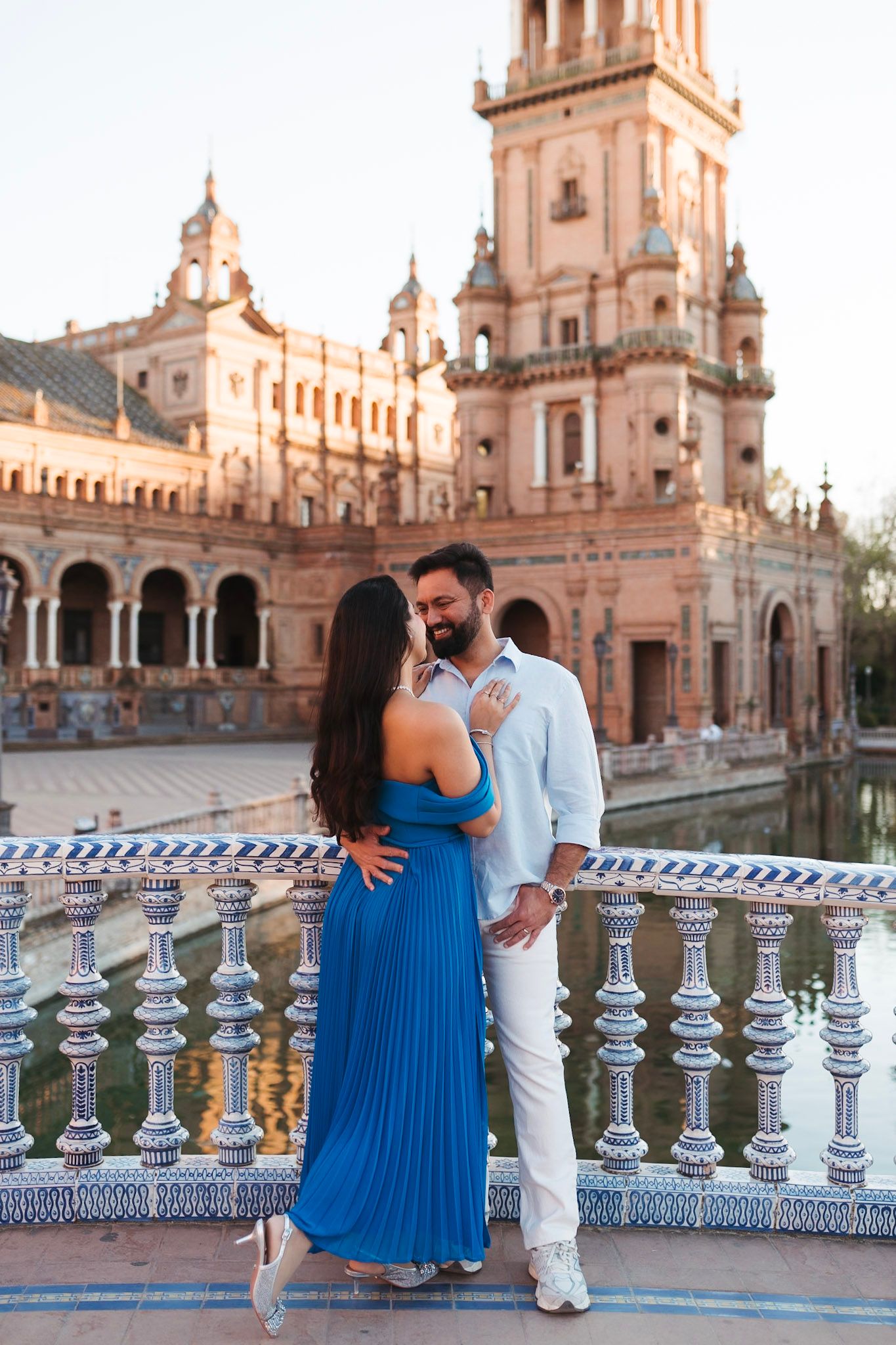 Romantic couple embracing on a tiled balcony at golden hour at Plaza de España, Seville, Spain.