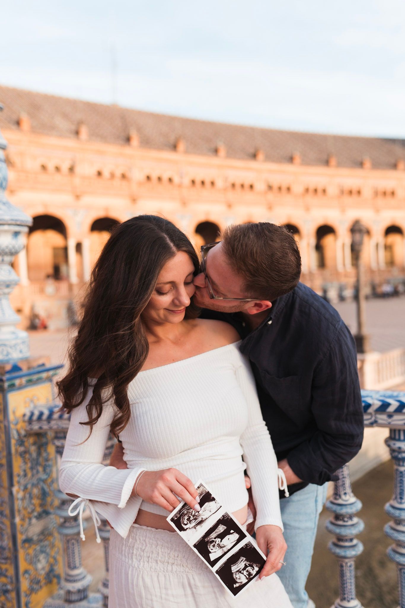 Couple shares tender moment holding ultrasound photos at Plaza de España, Seville.