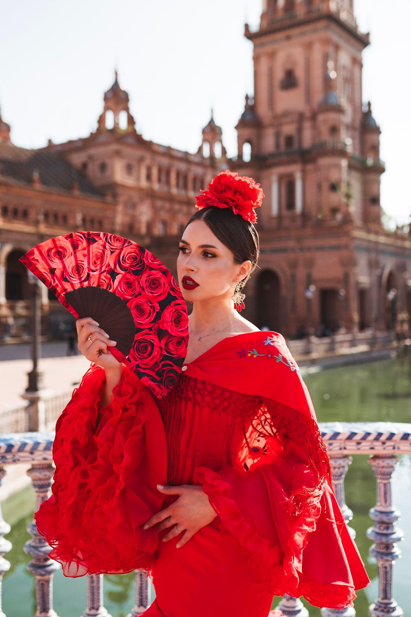 Flamenco dancer in red dress holding rose-decorated fan at Plaza de Espana, Seville.