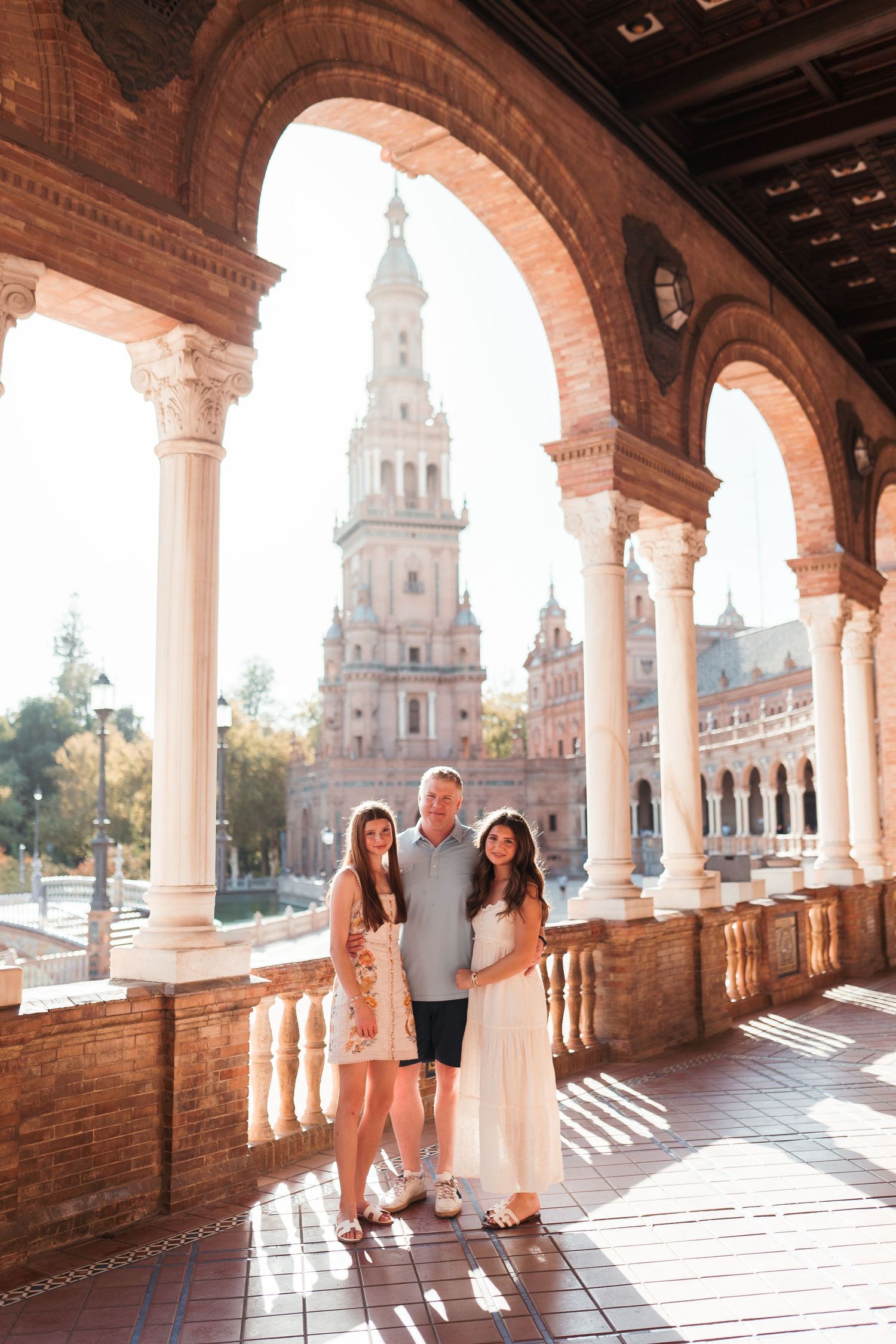 Family of three posing under arched colonnade at Plaza de España, Seville, Spain.