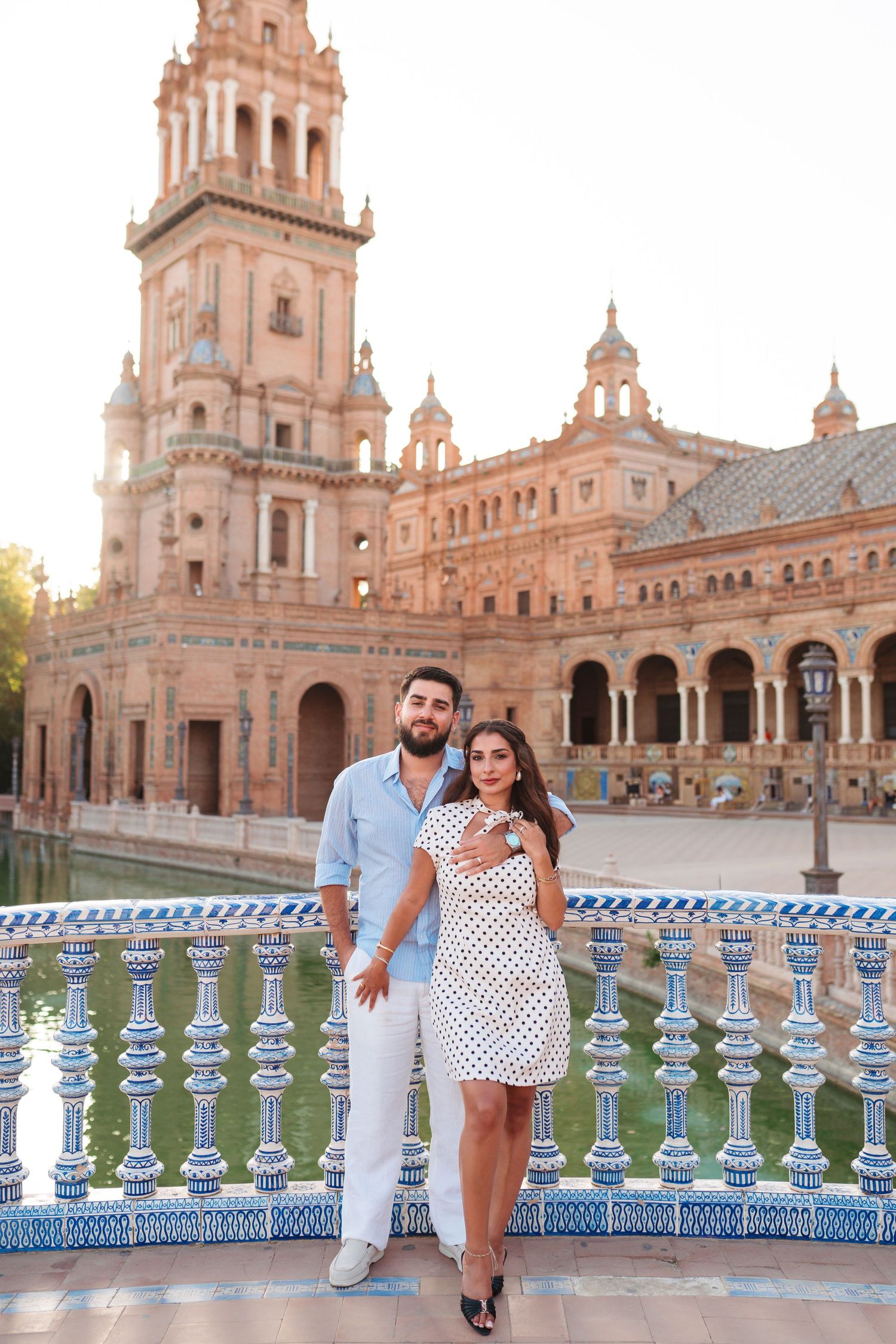 Couple posing at Plaza de España in Seville, Spain, with ornate architecture and blue tiled balustrade.