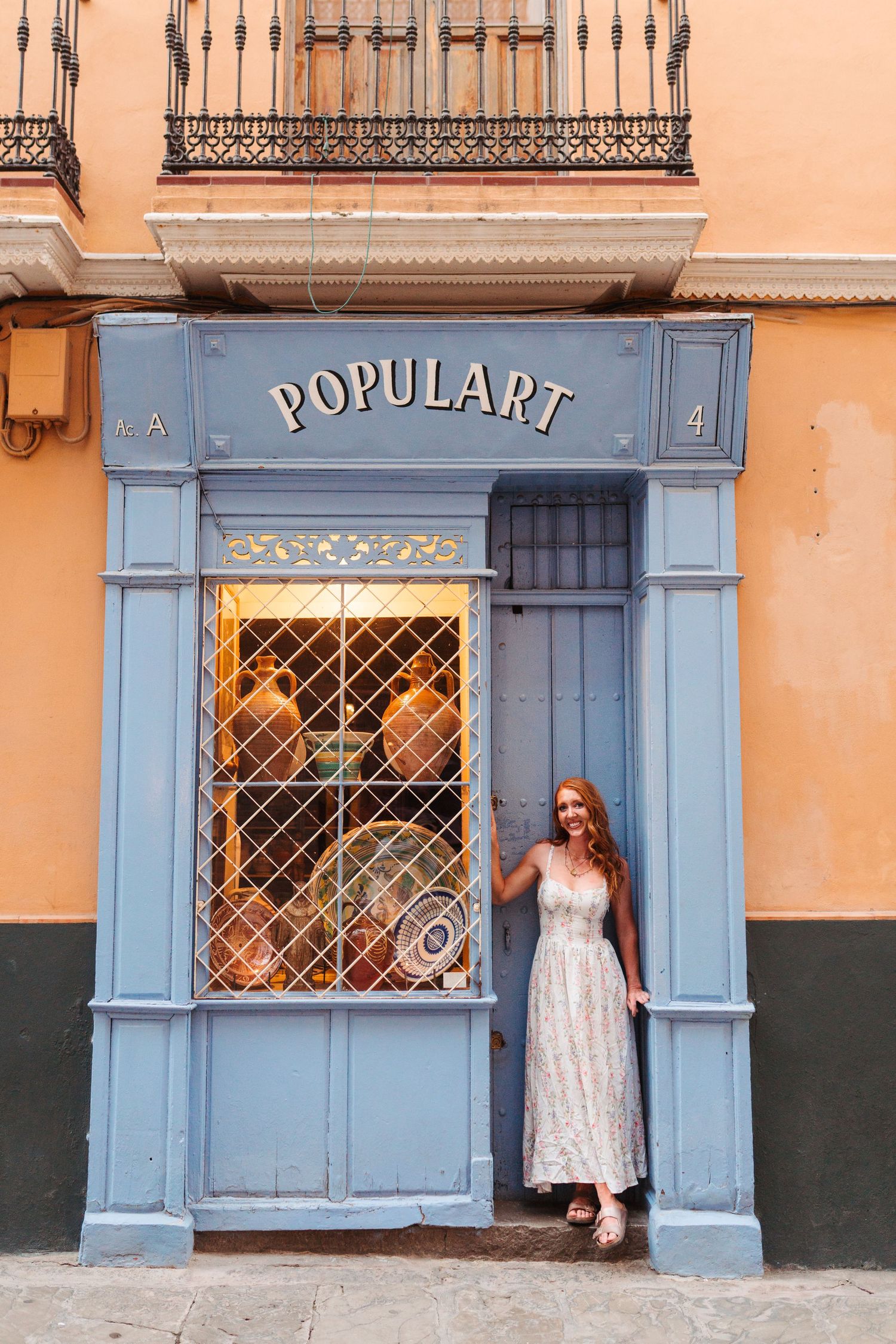 Woman in floral dress posing at entrance of Populart shop with blue facade on a charming European street.