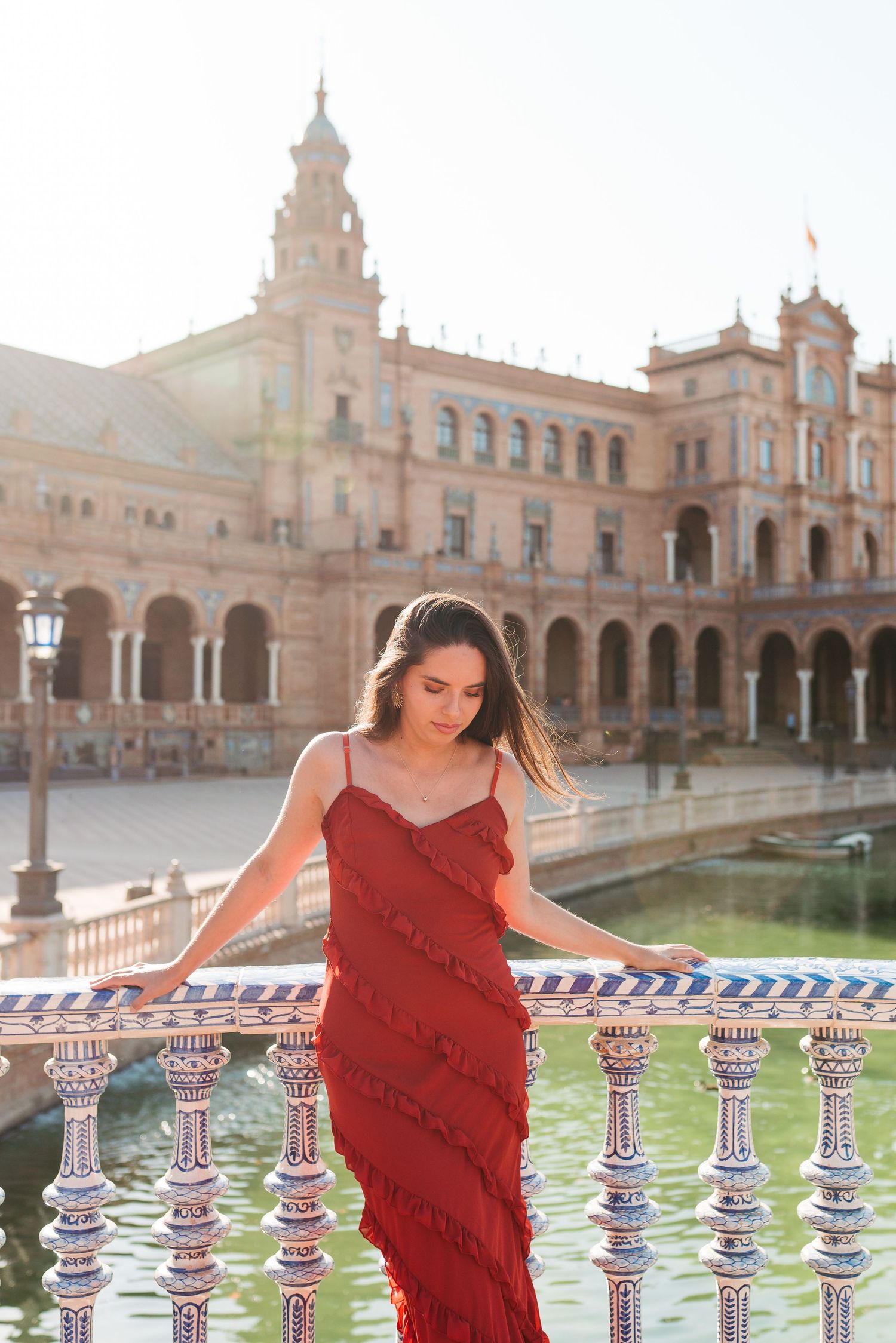 Woman in red fringe dress poses on ornate tiled bridge at Plaza de España, Seville, Spain.