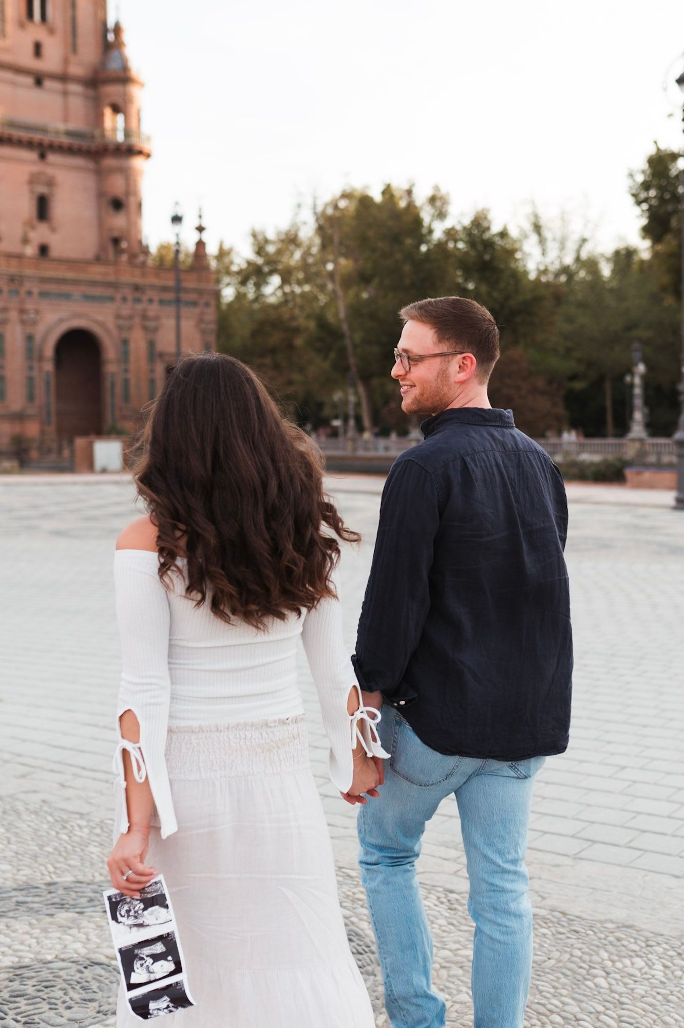 Couple walks holding hands and ultrasound photos at Plaza de España, Seville.