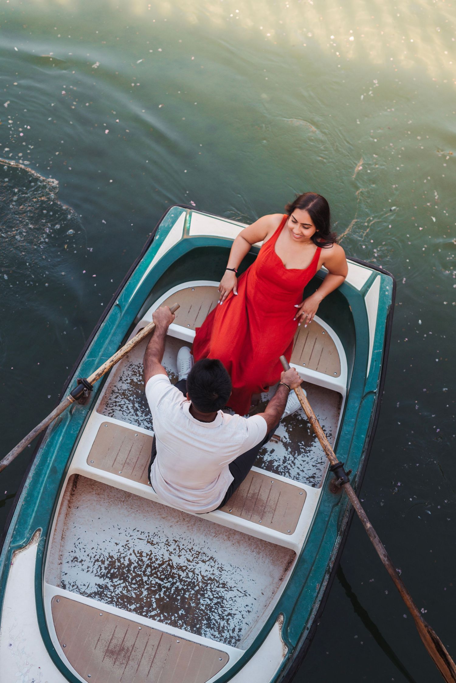 Aerial view of couple sharing romantic moment in vintage rowboat on calm water.
