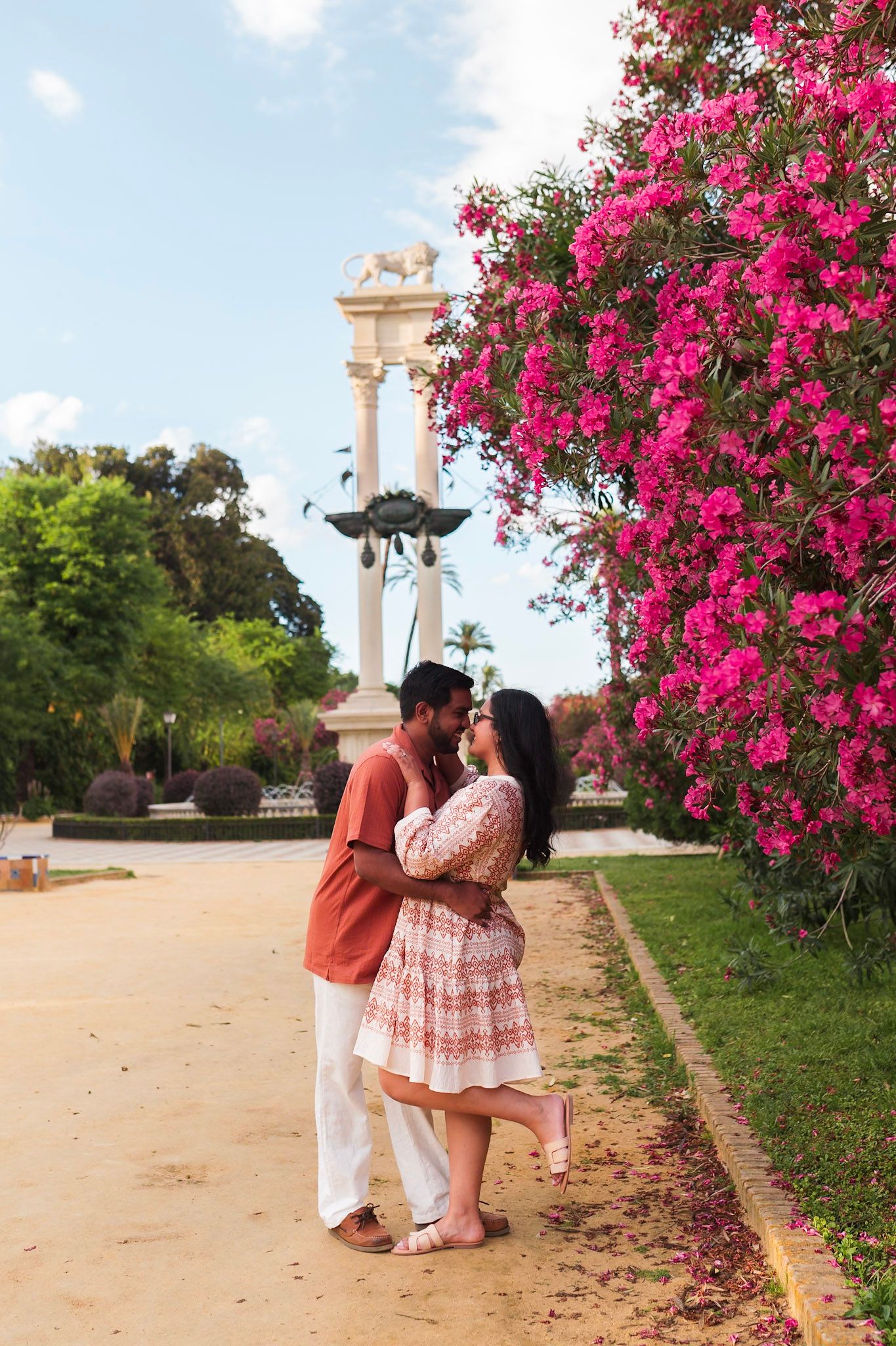 Couple kissing near vibrant pink bougainvillea flowers in sunny Seville park garden.
