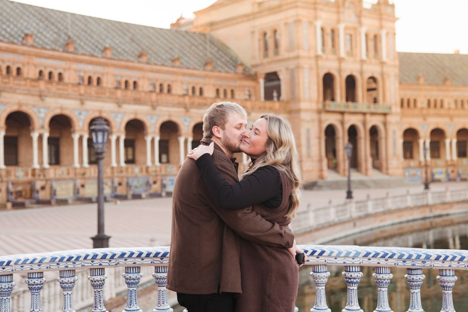 Newly engaged couple sharing a romantic embrace at Plaza de Espana in Seville, Spain.