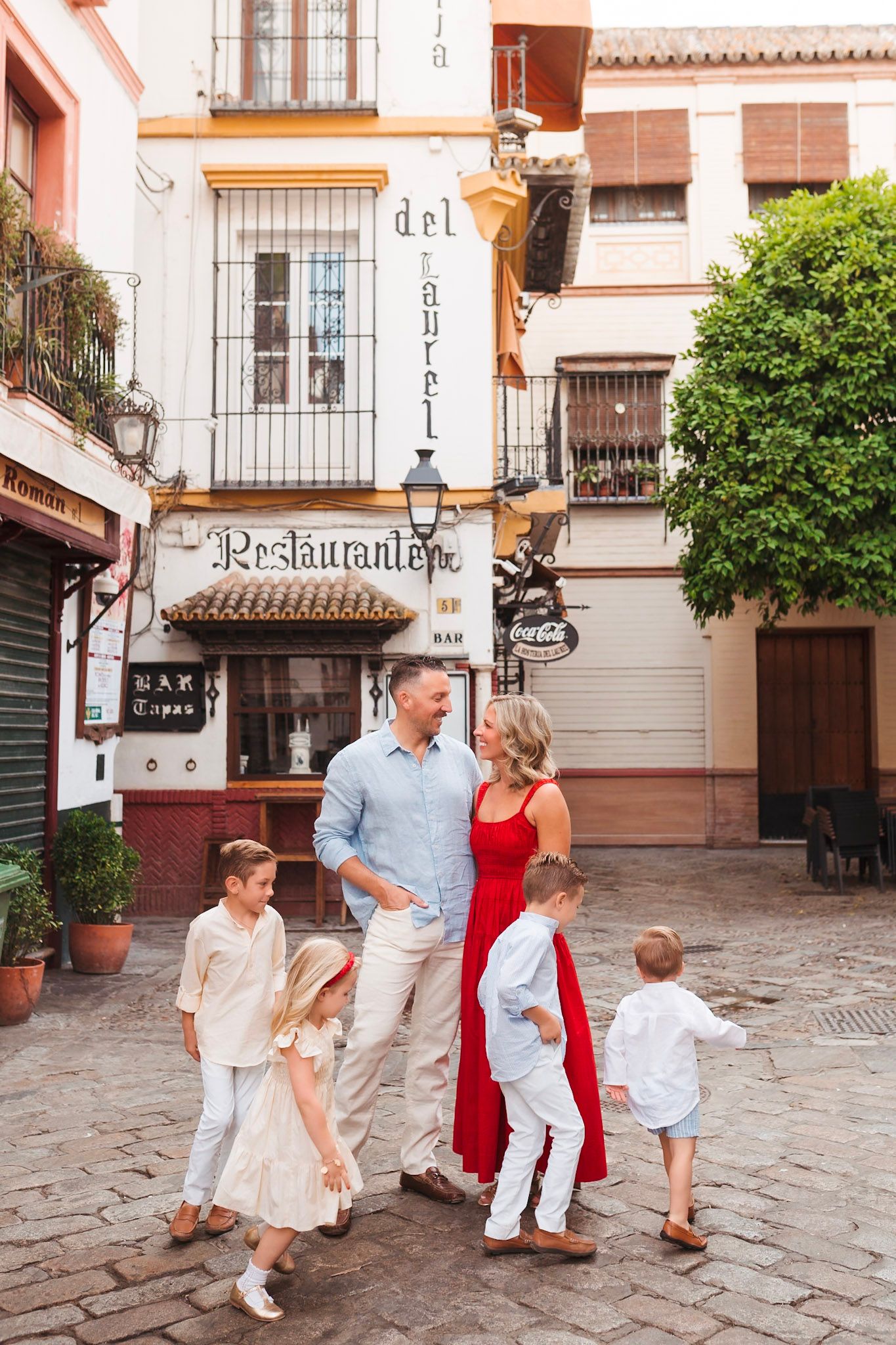 Family of six exploring a charming cobblestone street near a restaurant in Seville, Spain.