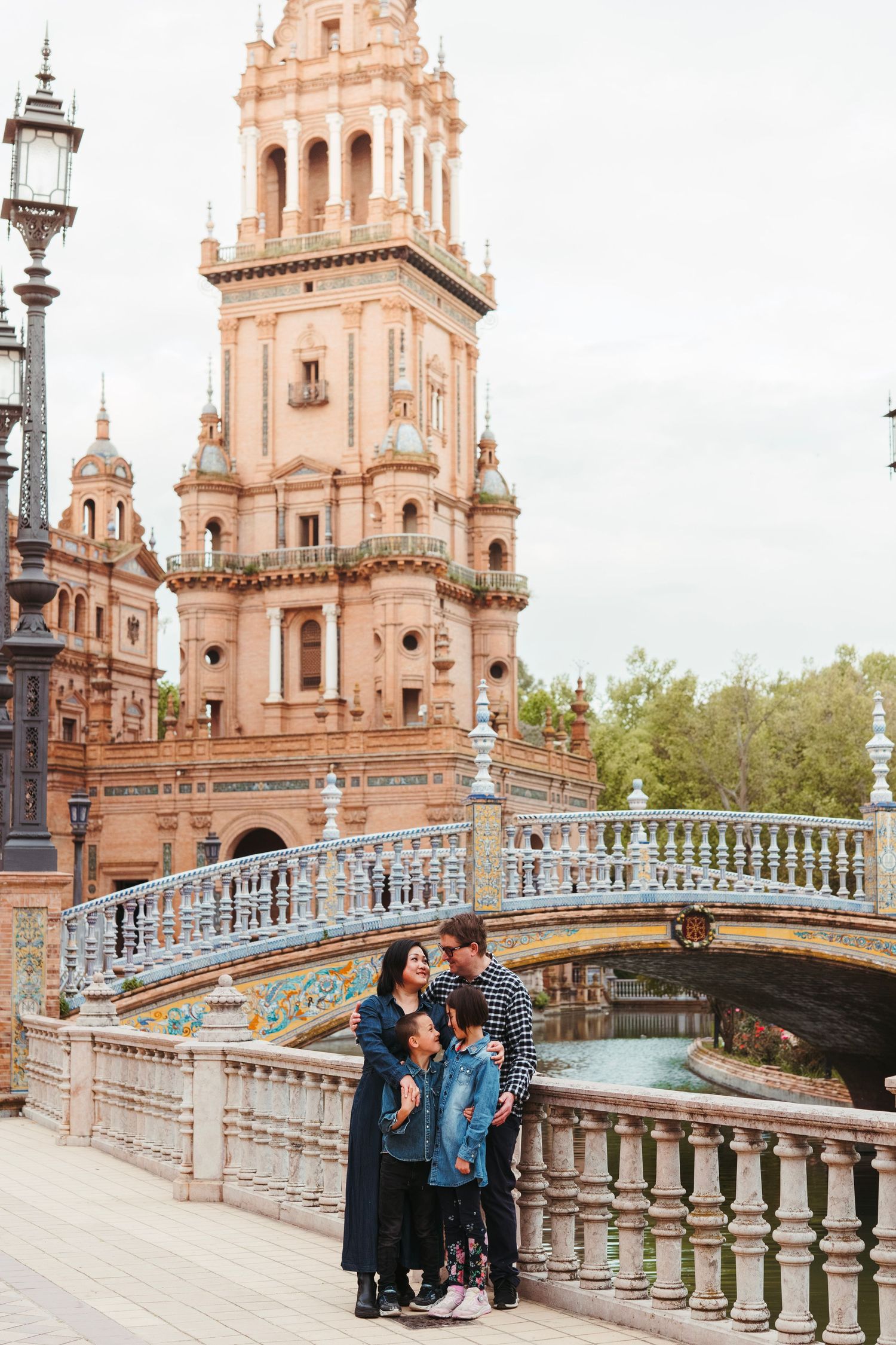 Family of three posing on a bridge at Plaza de España, Seville, with ornate tower backdrop.