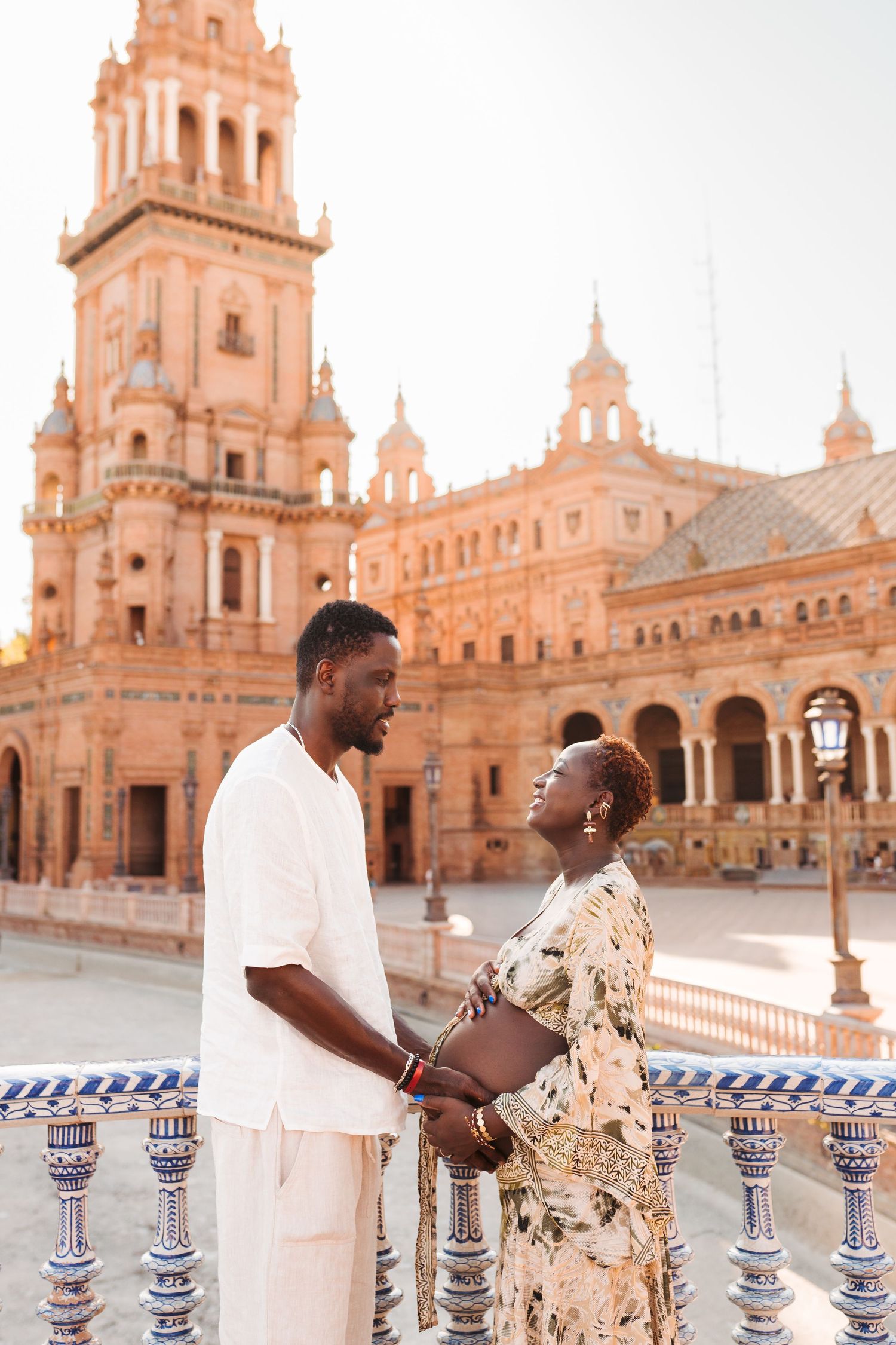 A couple holds hands at Plaza de España in Seville, Spain, with the ornate baroque architecture glowing at sunset.