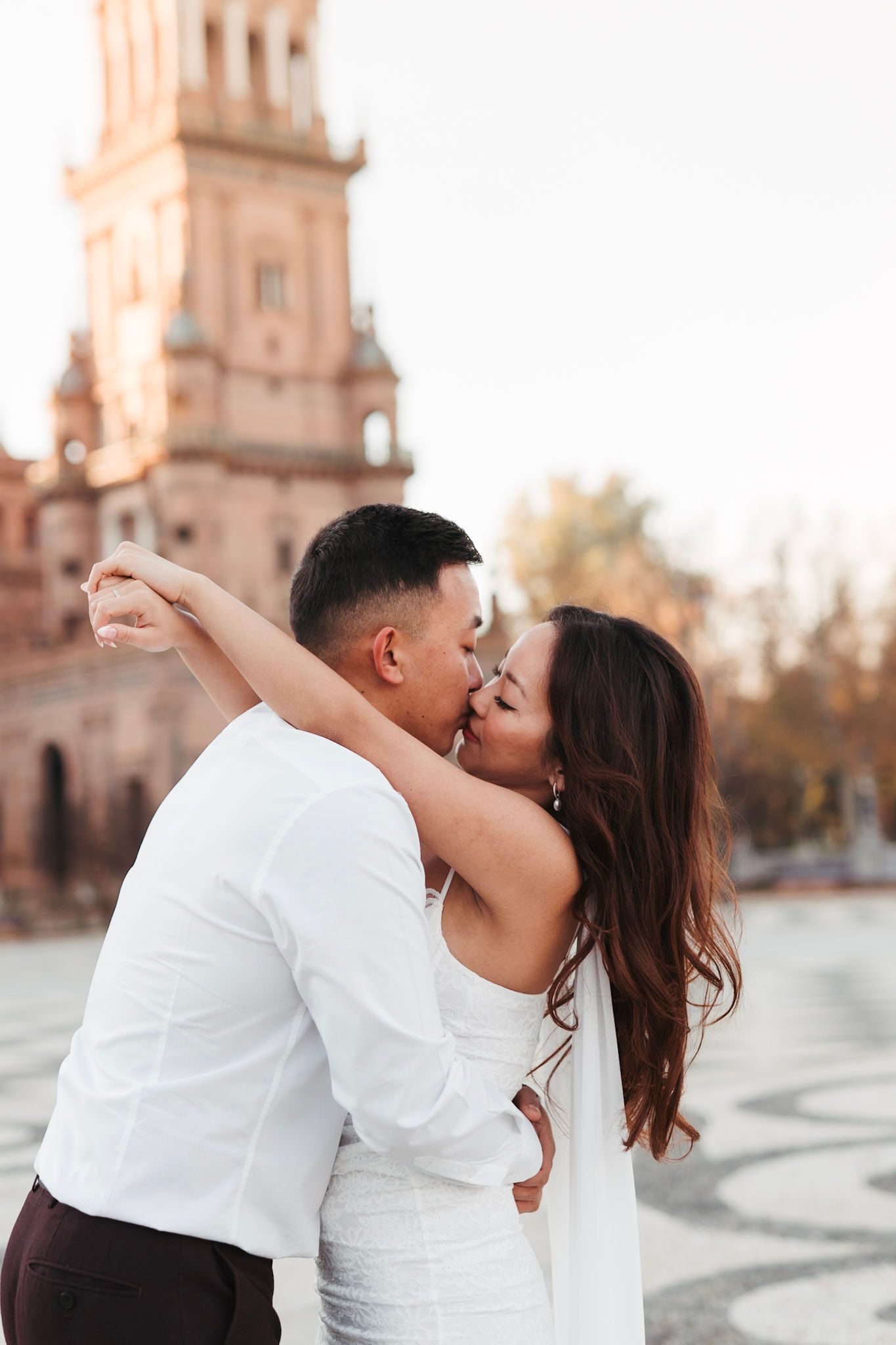 Couple sharing a passionate kiss at Plaza de España in Seville with tower backdrop.
