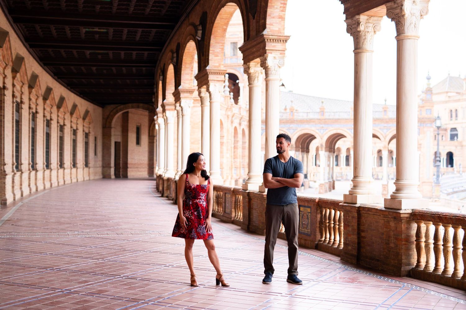 Couple strolling through elegant arched colonnade gallery at Plaza de España in Seville, Spain.