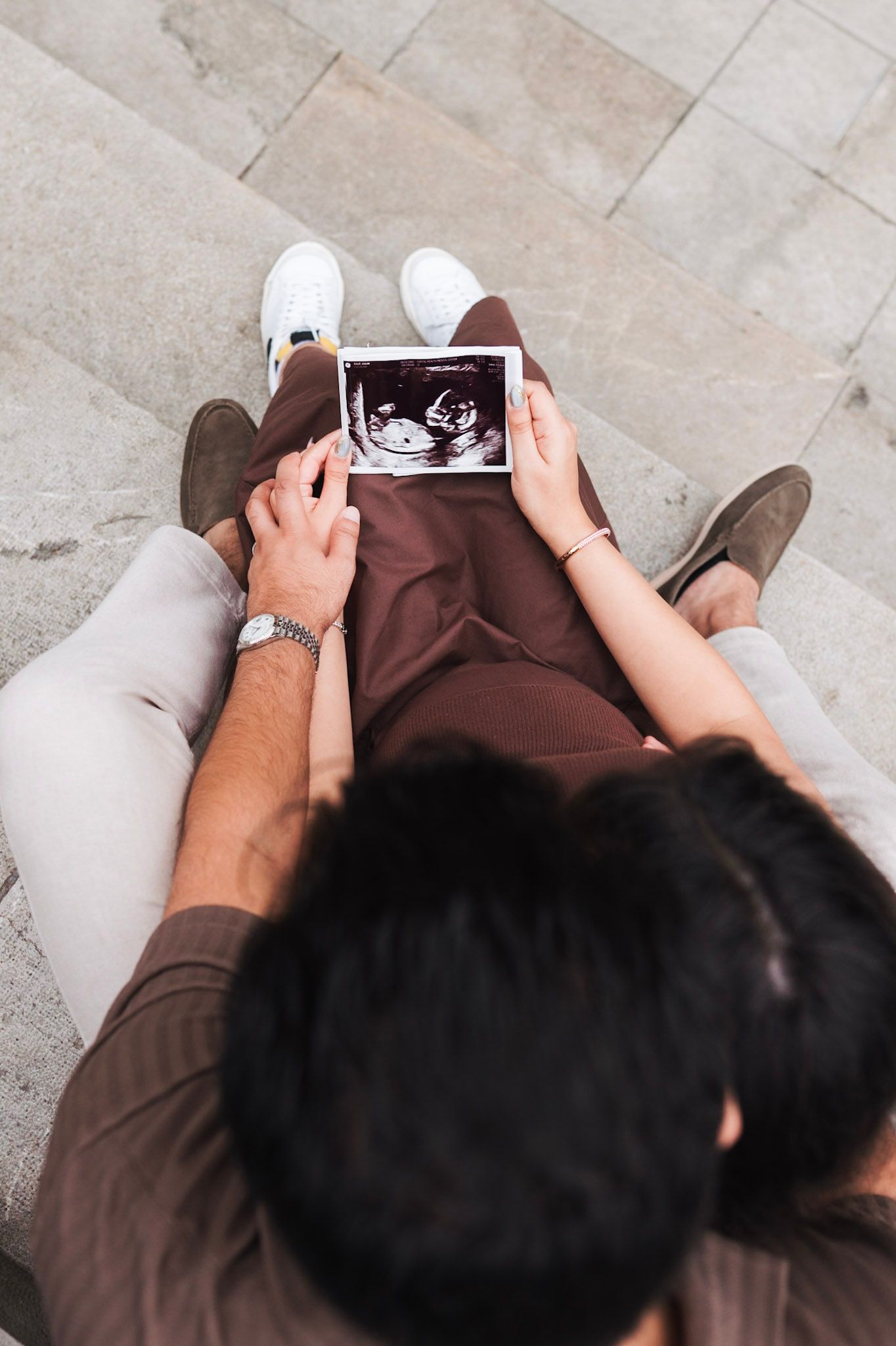 Overhead view of couple sitting together reviewing baby ultrasound photograph.