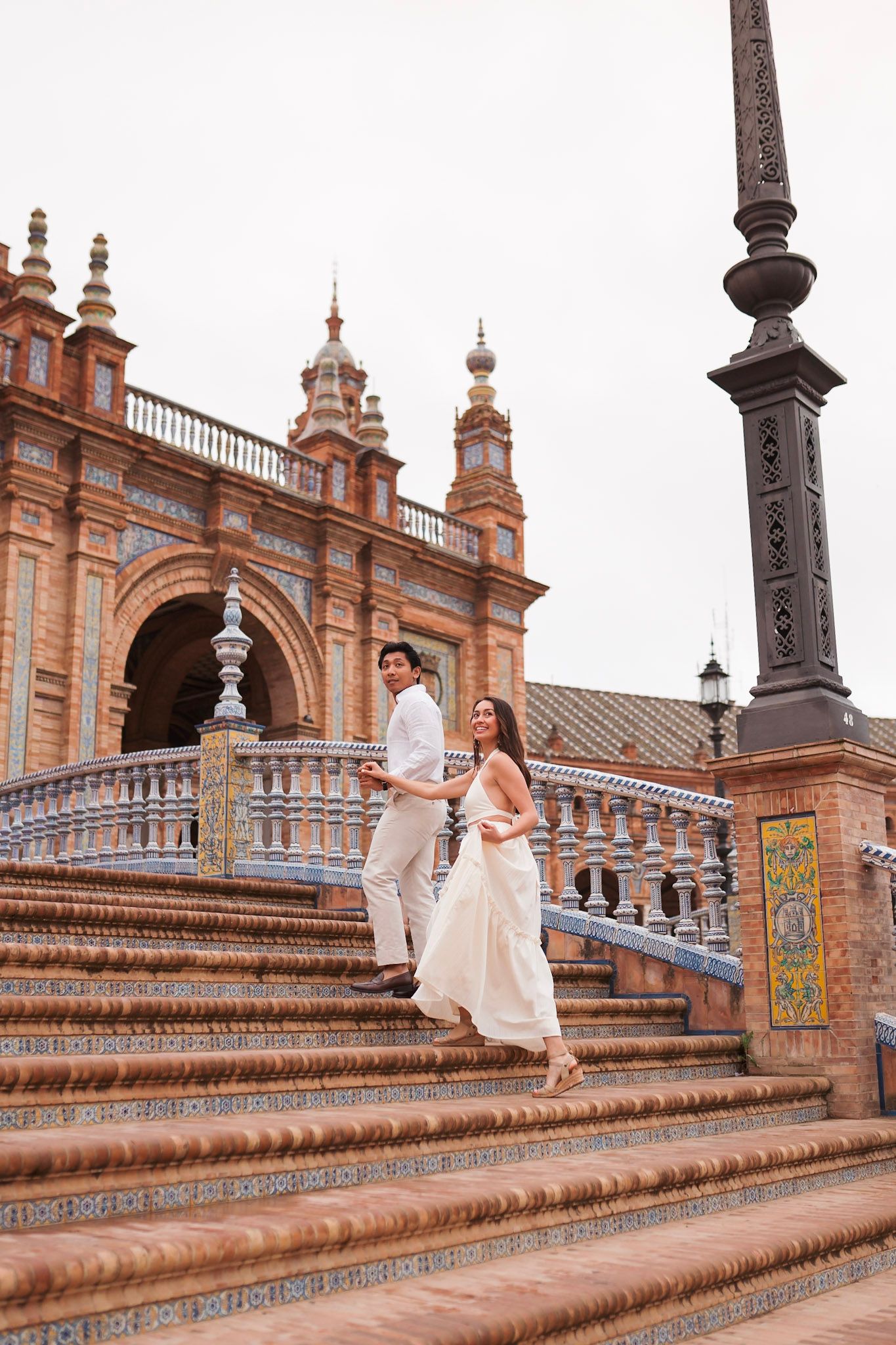 Couple descending ornate steps at Plaza de España in Seville, Spain, woman in flowing white dress.