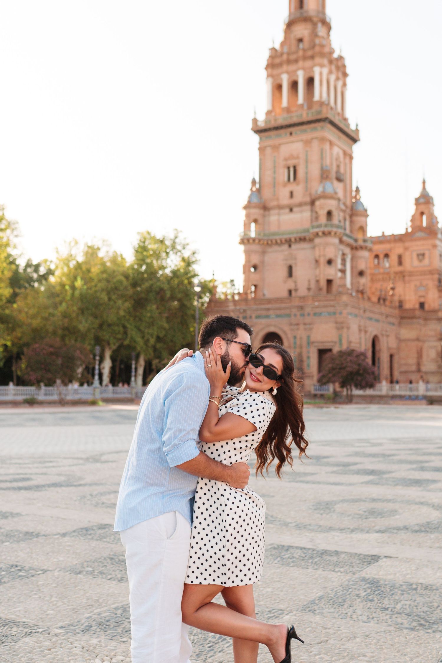 Romantic couple embracing and kissing at Plaza de España in Seville, Spain, woman in polka dot dress and sunglasses.