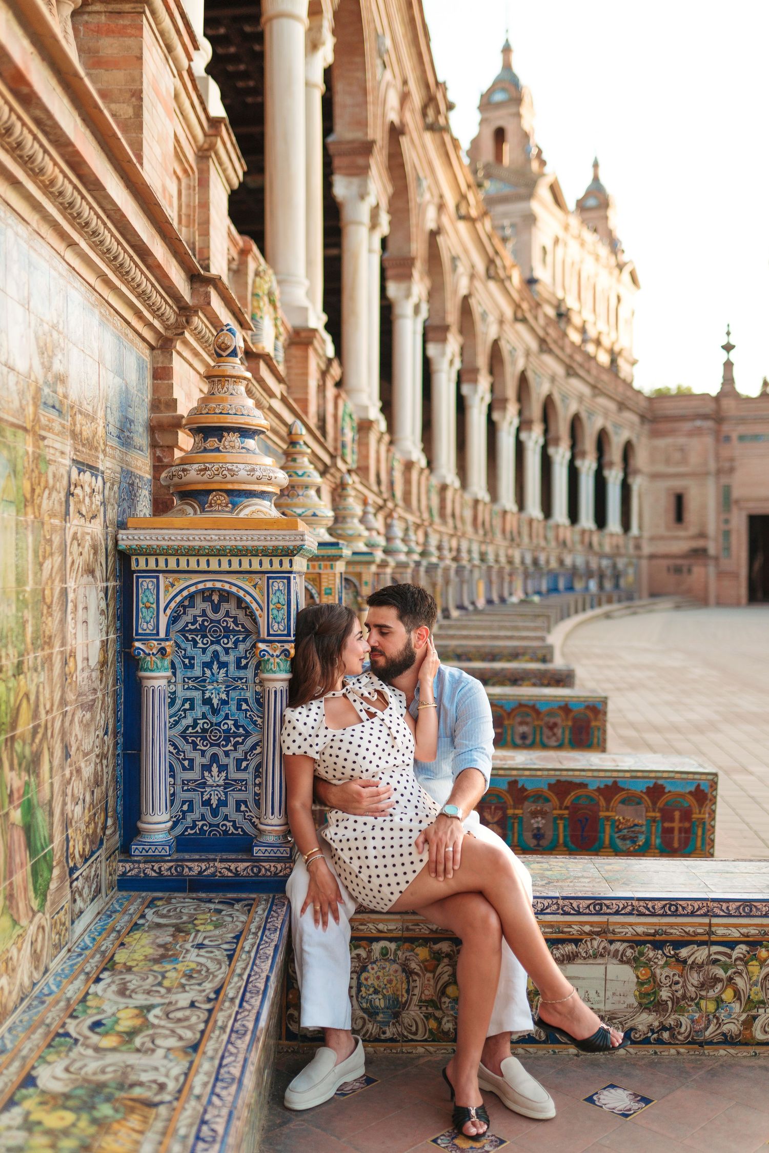 Romantic couple sharing a kiss on ornate tiled bench at Plaza de Espana, Seville, Spain.