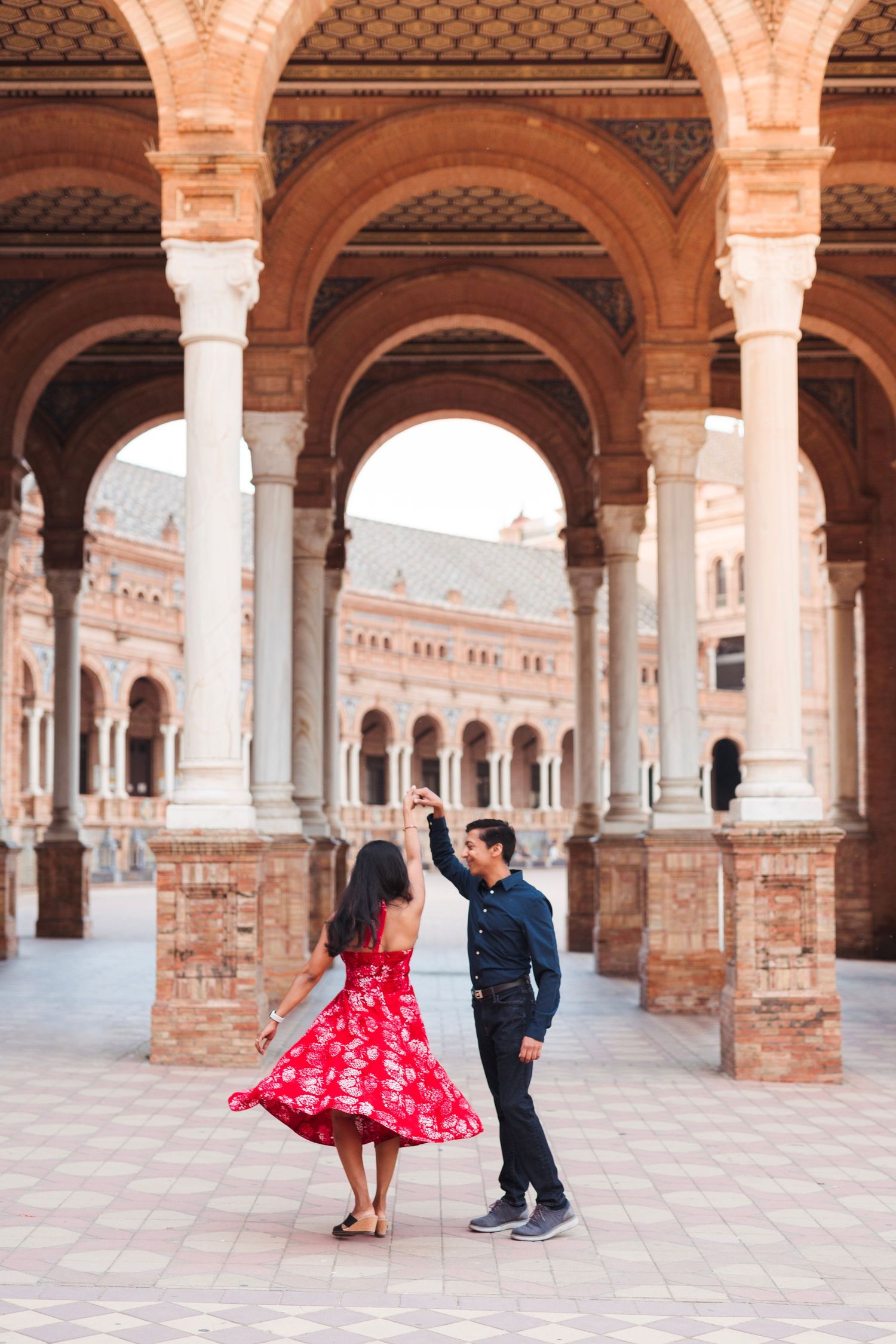 Couple dancing joyfully under arched colonnade at Plaza de Espana in Seville Spain.