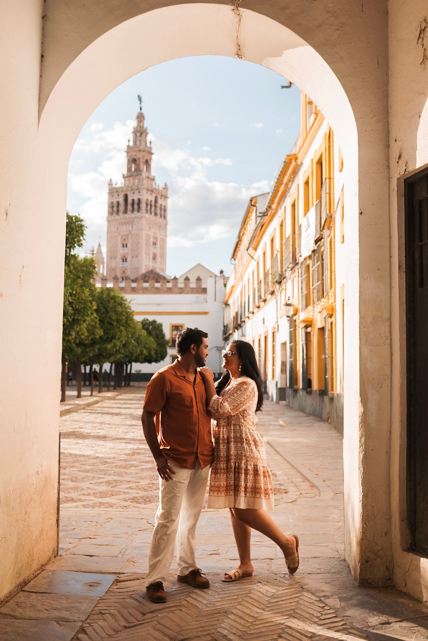 Romantic couple facing each other under stone arch with Giralda tower in Seville.
